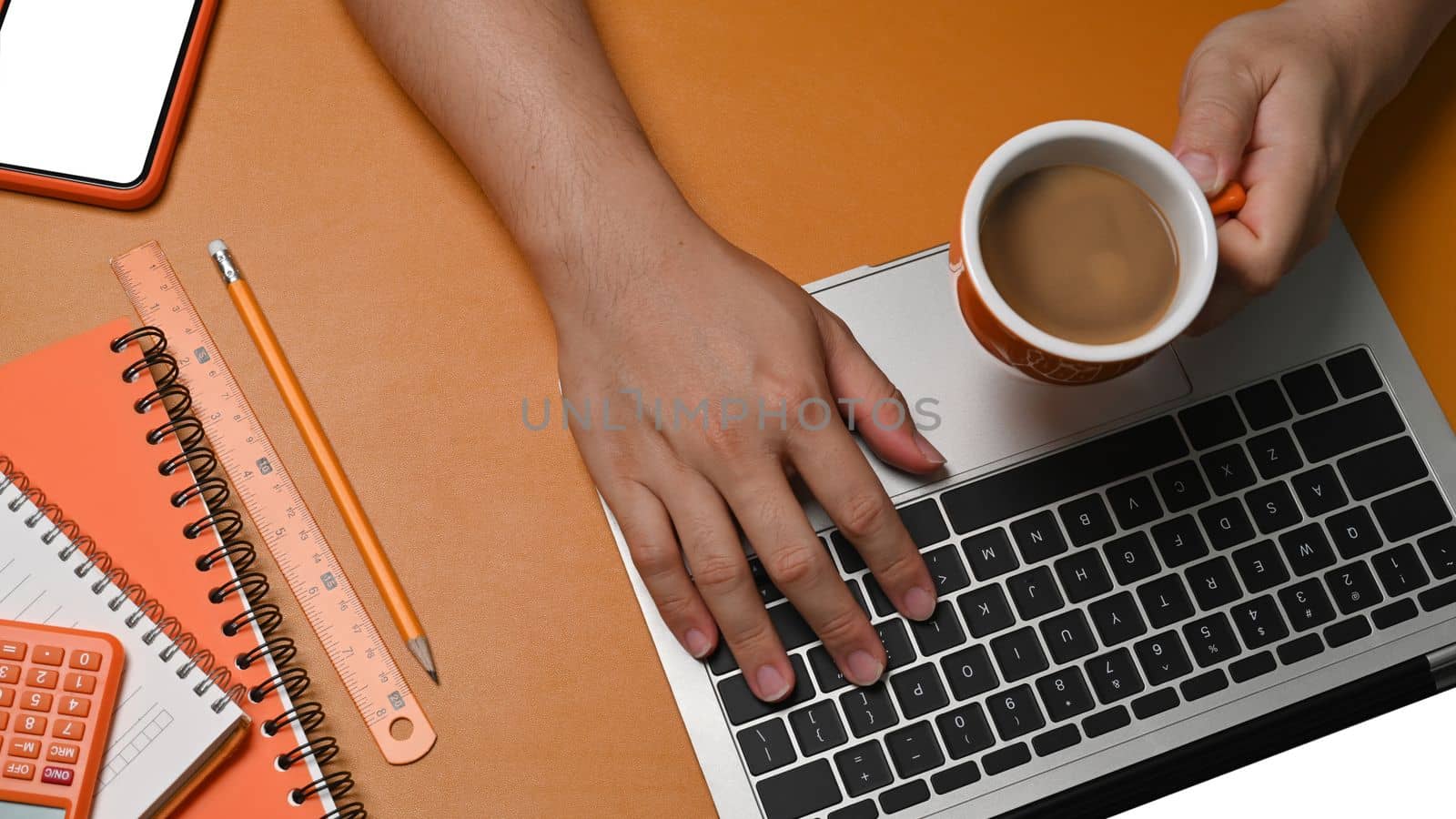 Man holding coffee cup and using laptop computer on brown leather.