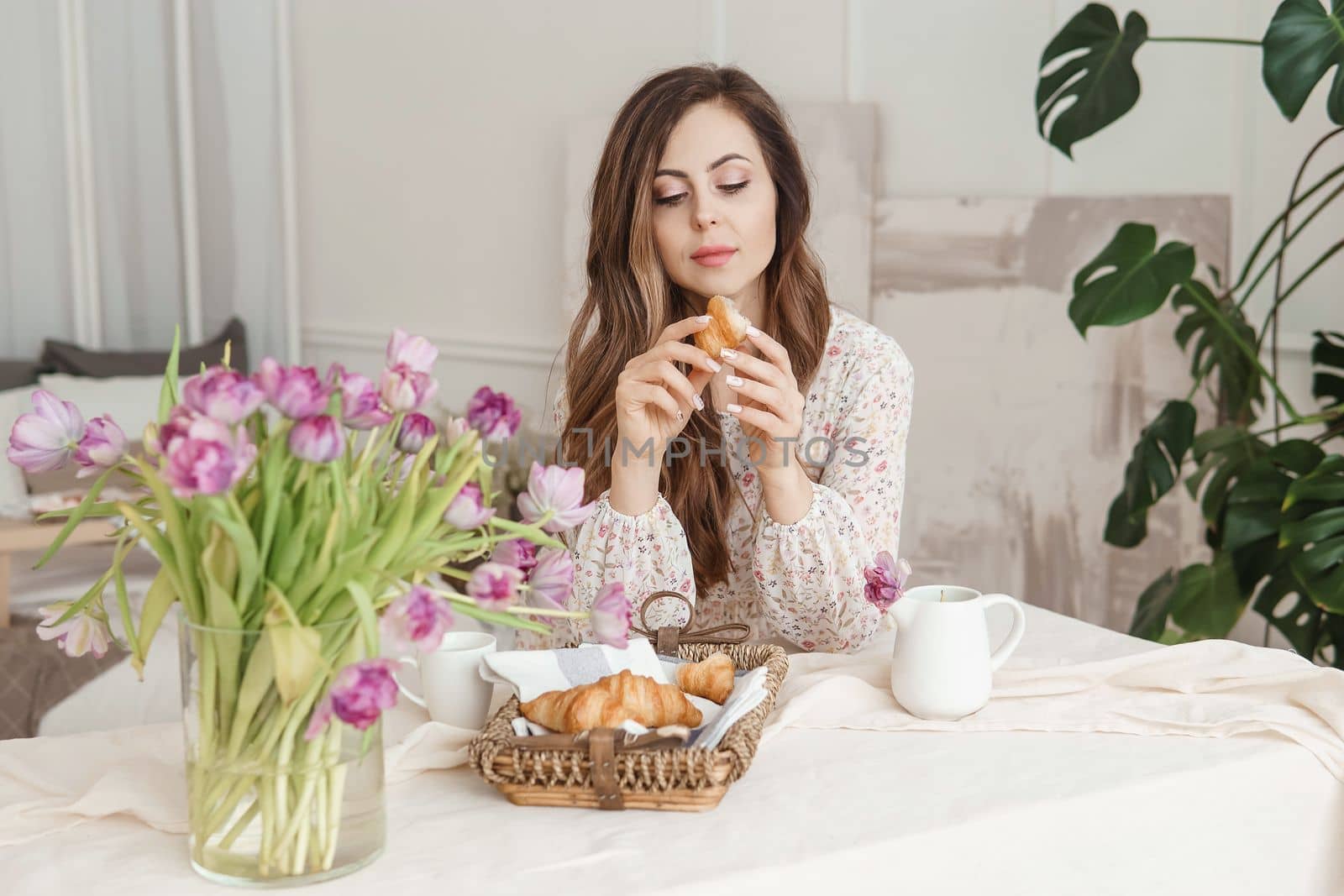 A brown-haired woman with long hair is having breakfast at the table with croissants and a cup of coffee. Spring portrait