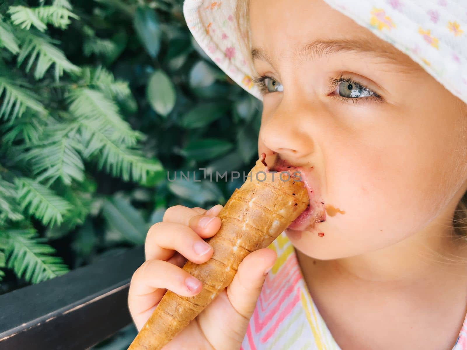 Little girl in a panama hat bites a popsicle in a waffle cone. High quality photo