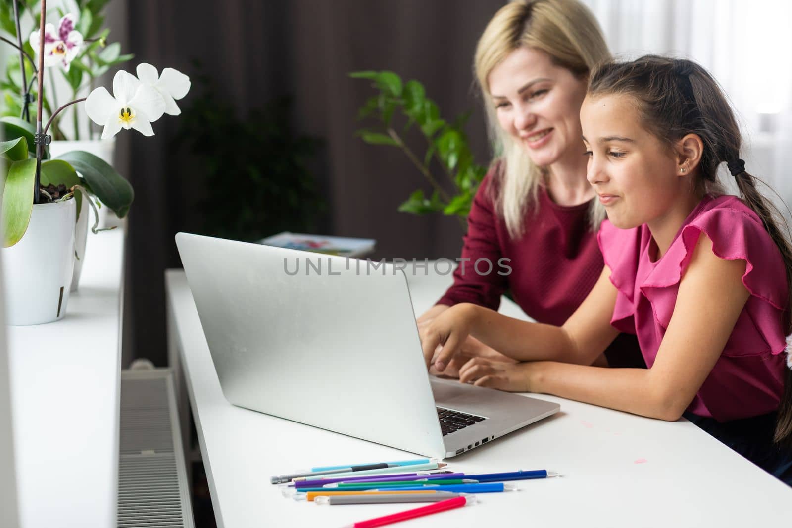 Happy teacher and student girl sitting at working desk in classroom. Cheerful young mother and child sitting at table and smiling. Little kid and her private language tutor.