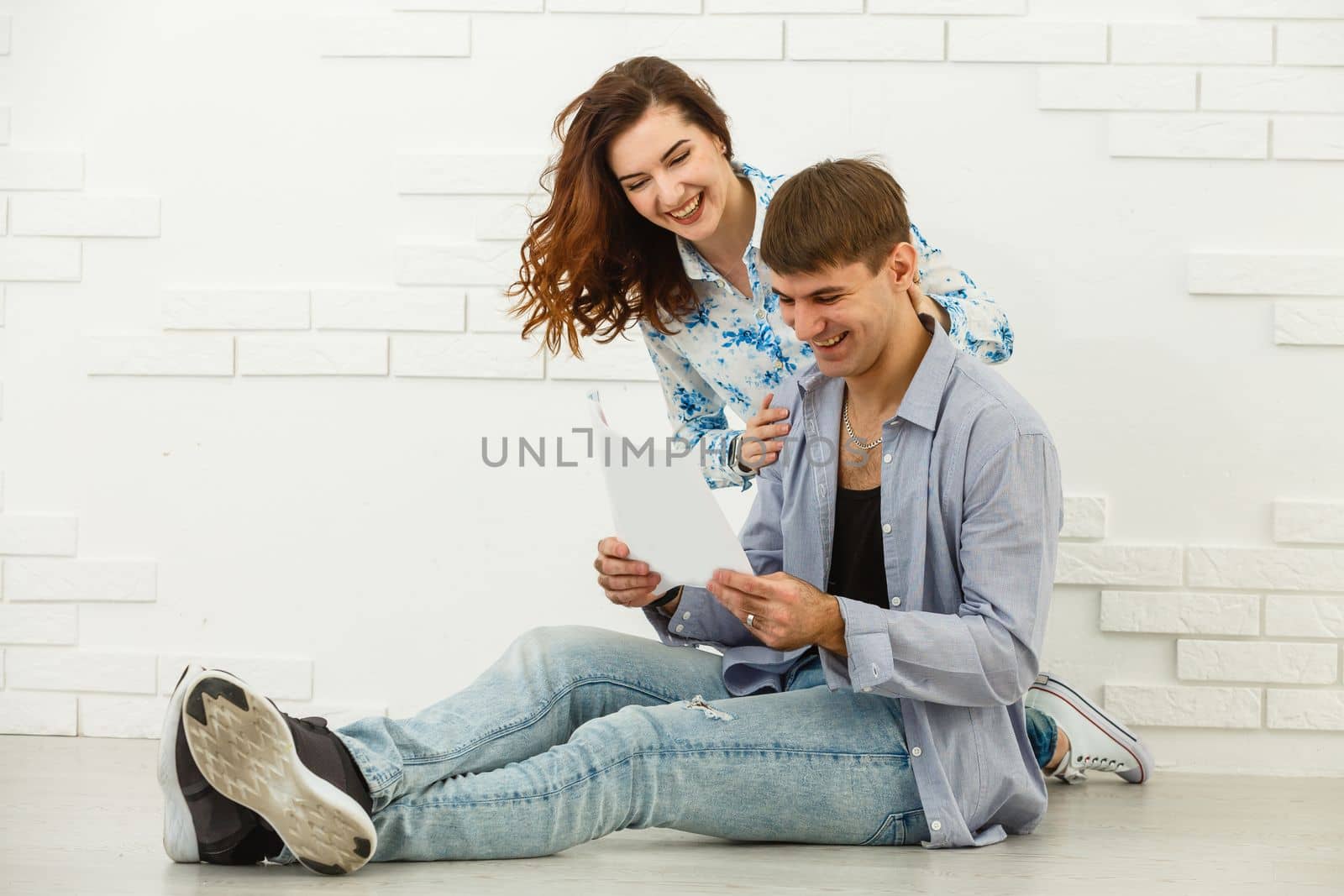 Smiling husband and wife sit taking care of utility bills and house maintenance documents, happy young couple read paperwork by Andelov13