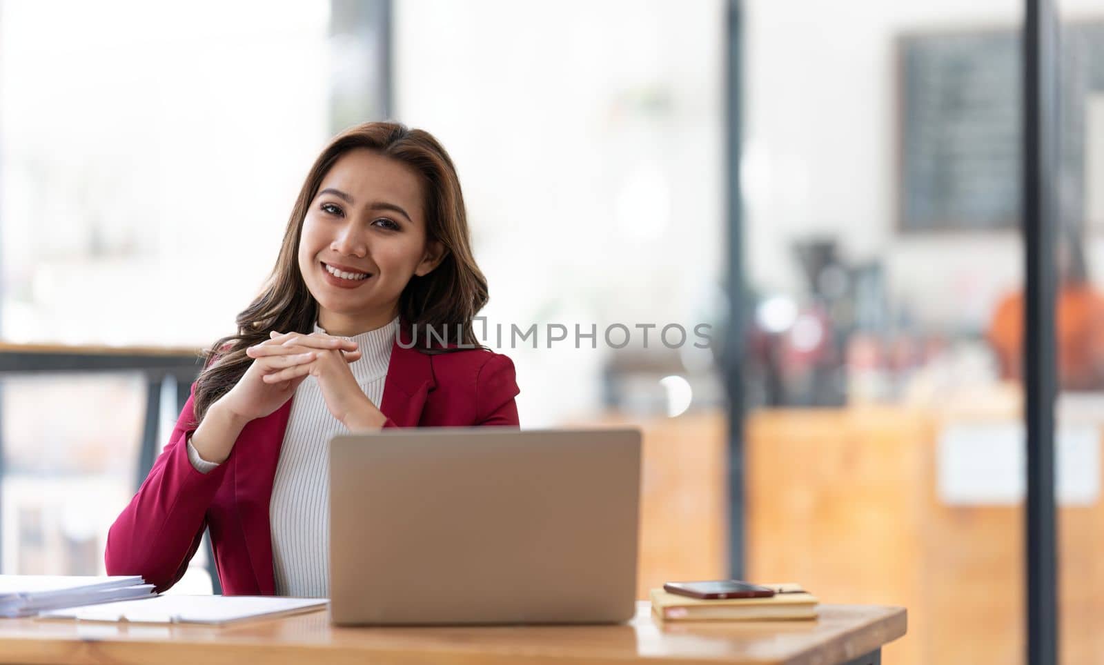 Young businesswoman working at her laptop and going over paperwork while sitting at a desk in an office by nateemee