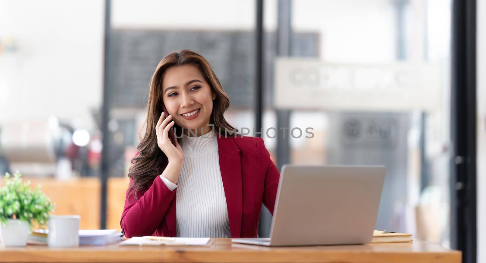 Smiling beautiful Asian businesswoman analyzing chart and graph showing changes on the market and holding smartphone at office by nateemee