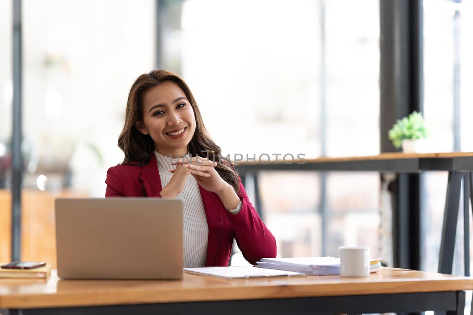 Young businesswoman working at her laptop and going over paperwork while sitting at a desk in an office.