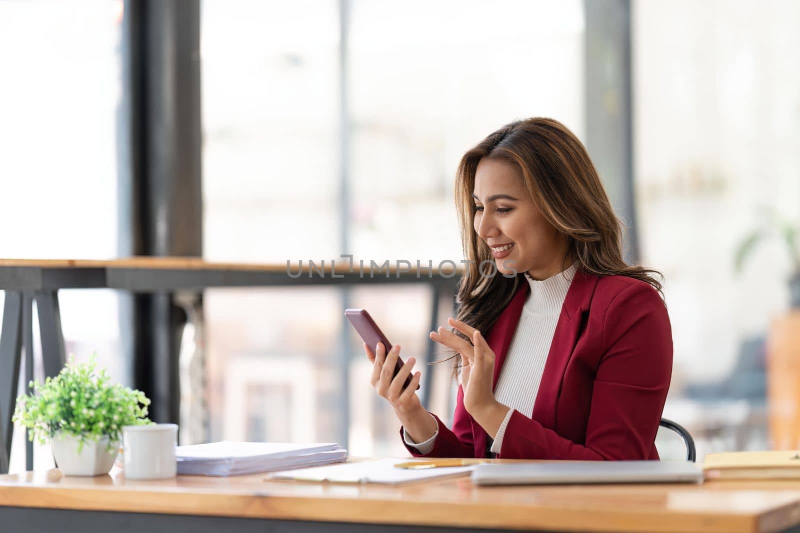 Happy businesswoman using mobile phone while working at office with laptop by nateemee