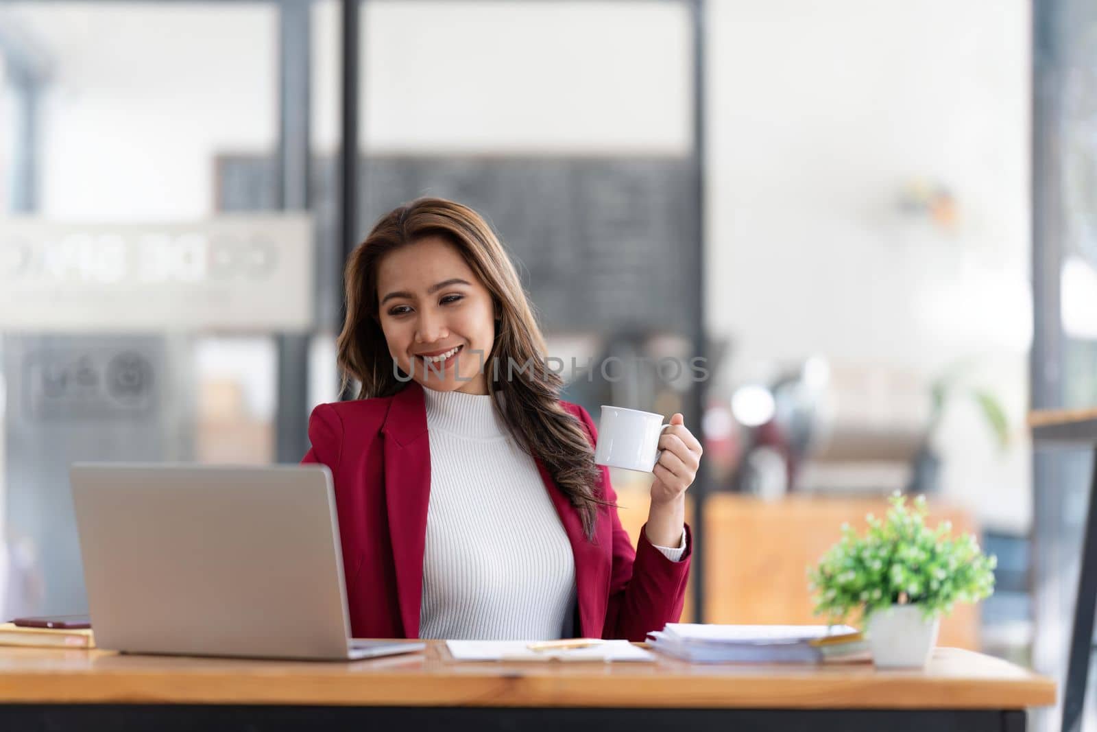 Young Asian businesswoman working and holding hot coffee cup in the office room by nateemee