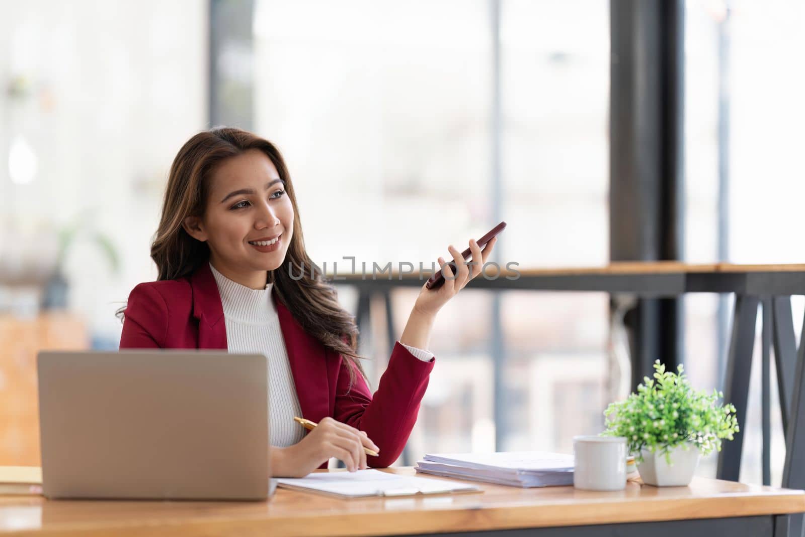 Happy businesswoman using mobile phone while working at office with laptop.