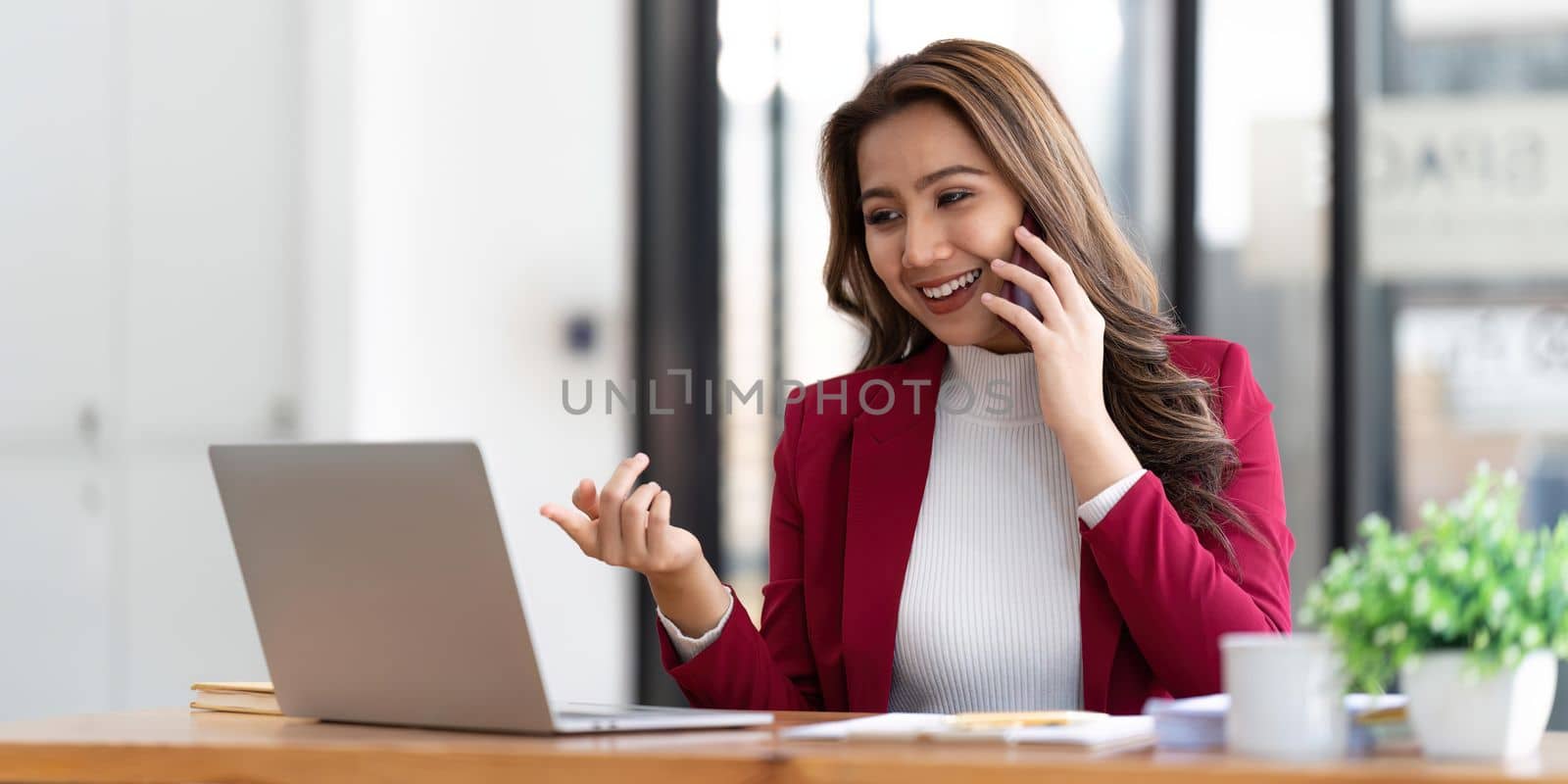 Smiling beautiful Asian businesswoman analyzing chart and graph showing changes on the market and holding smartphone at office.