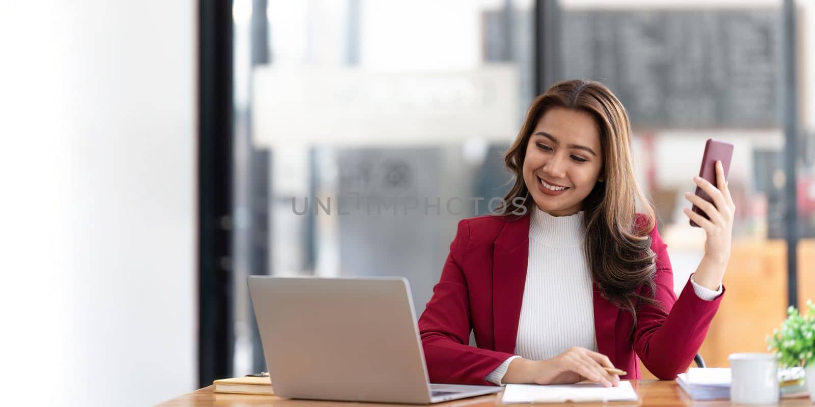 Smiling beautiful Asian businesswoman analyzing chart and graph showing changes on the market and holding smartphone at office by nateemee