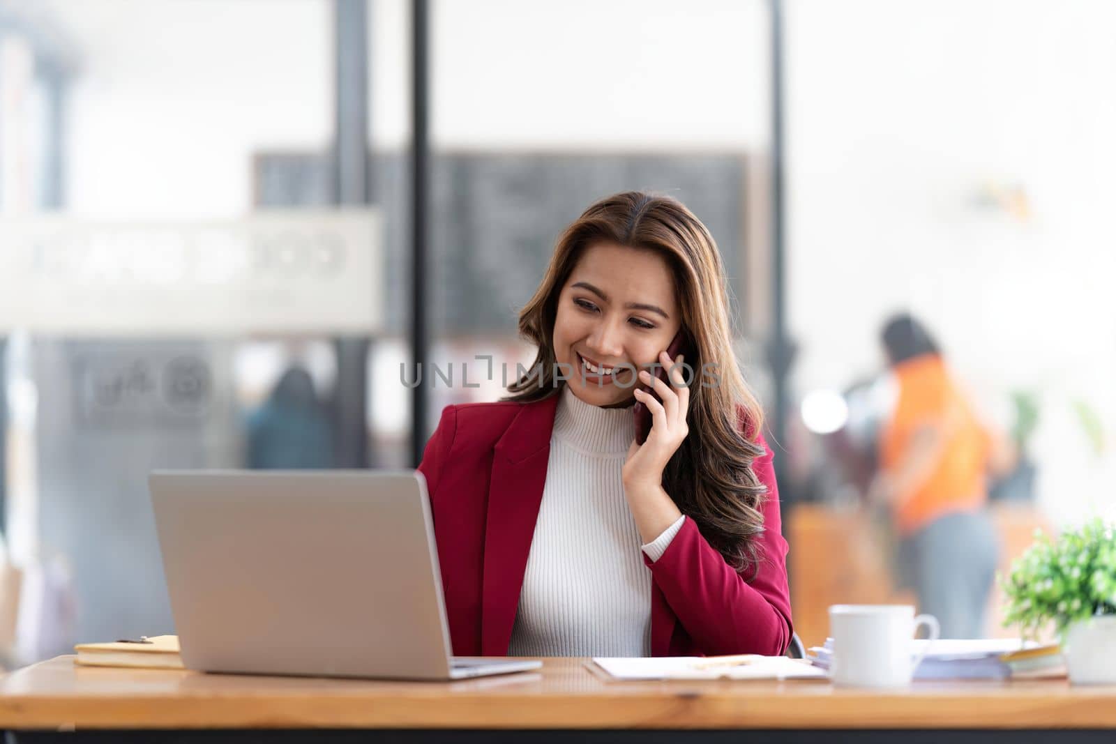 Smiling beautiful Asian businesswoman analyzing chart and graph showing changes on the market and holding smartphone at office by nateemee