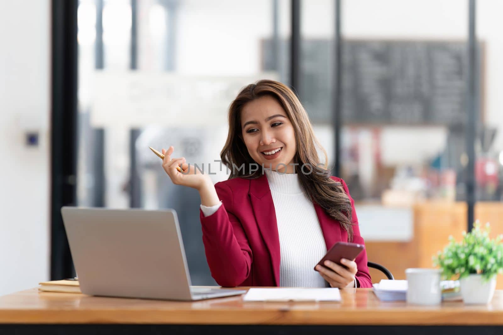 Smiling beautiful Asian businesswoman analyzing chart and graph showing changes on the market and holding smartphone at office by nateemee