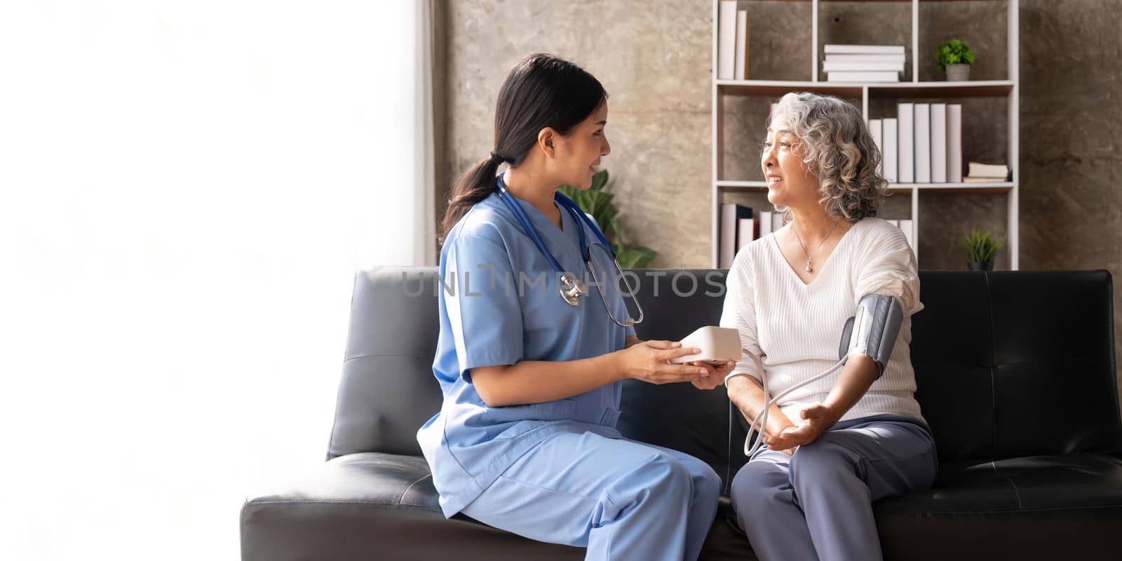 Happy senior woman having her blood pressure measured in a nursing home by her caregiver. Happy nurse measuring blood pressure of a senior woman by nateemee