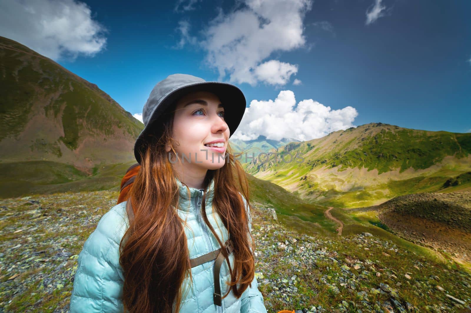 Portrait of a smiling woman resting during a mountain hike. A woman with a backpack enjoys the view while standing in the mountains. Happy tourist by yanik88