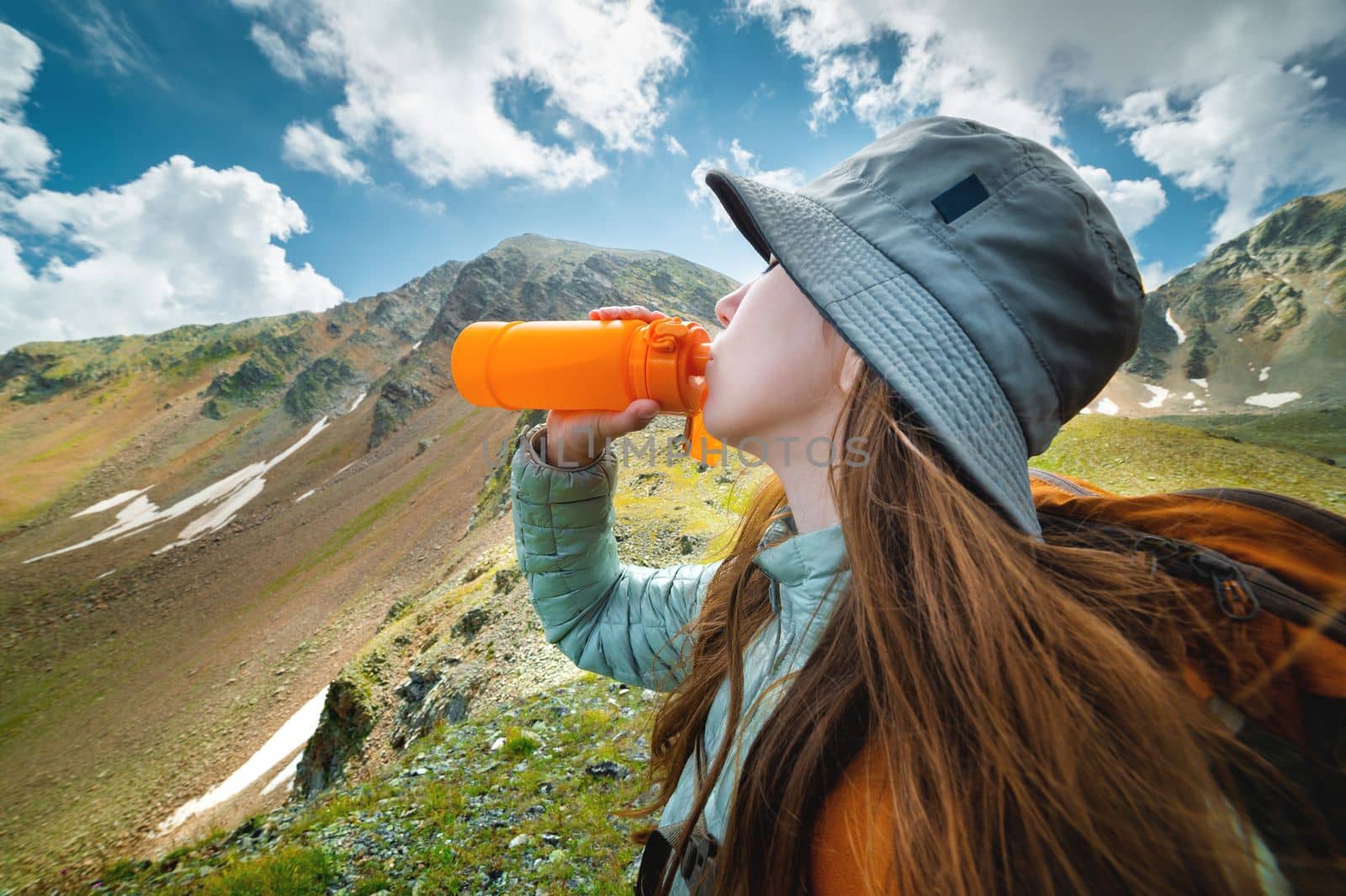 Healthy female hiker drinks water on a hike in nature. Beautiful young woman happy on a hike with a bottle of water taking a break.