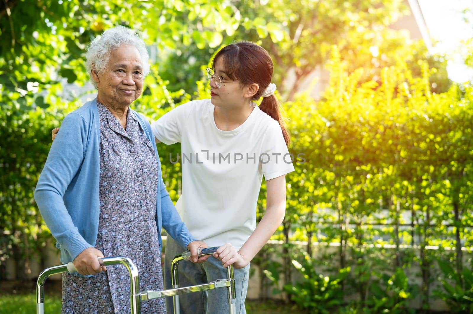 Caregiver help Asian elderly woman patient walk with walker in park, healthy strong medical concept.