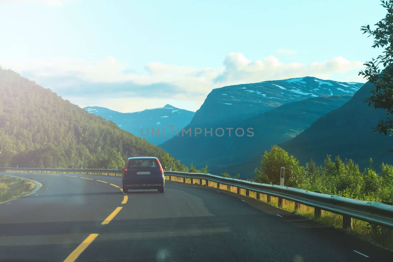 journey to the north, a small car rides against the backdrop of snow-capped mountains , summer evening