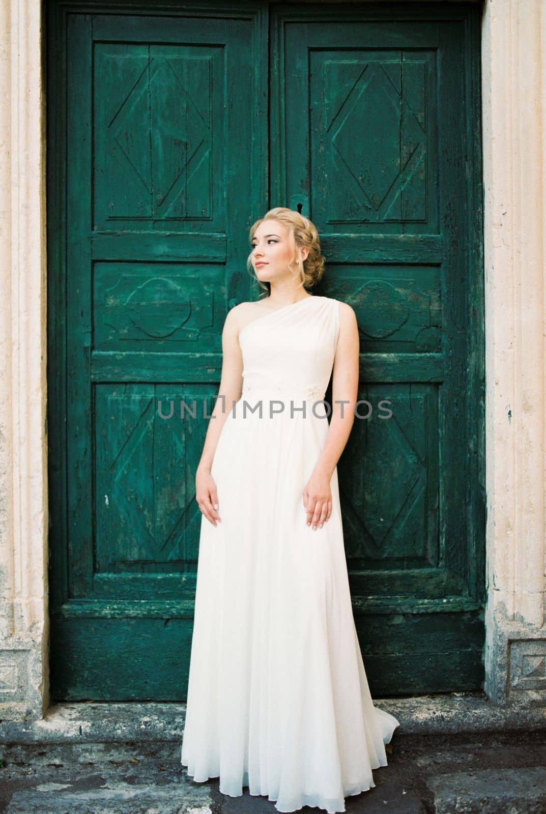 Bride in a white dress stands leaning against a green door. High quality photo