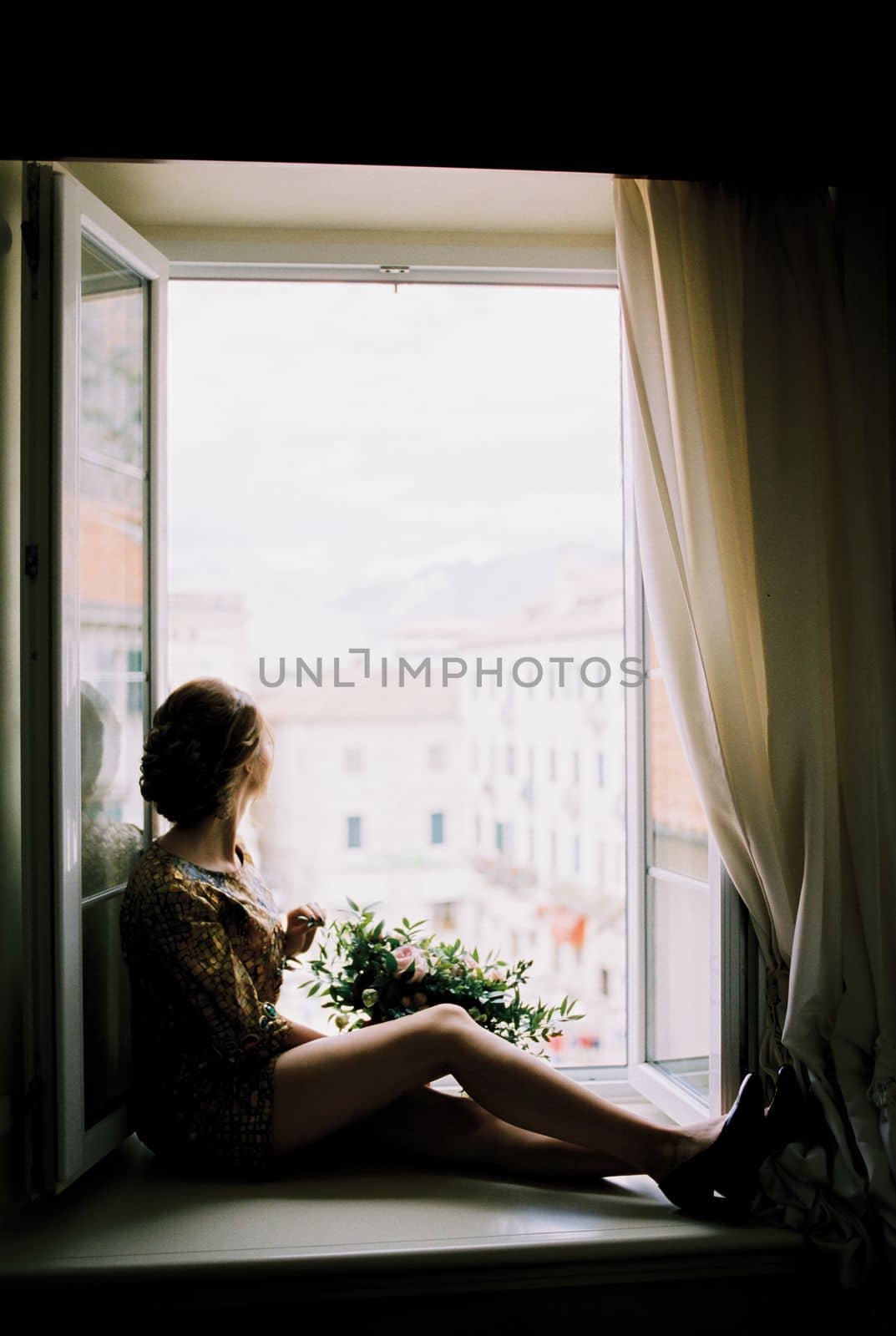 Woman with a bouquet of flowers sits on the windowsill and looks out the open window. High quality photo