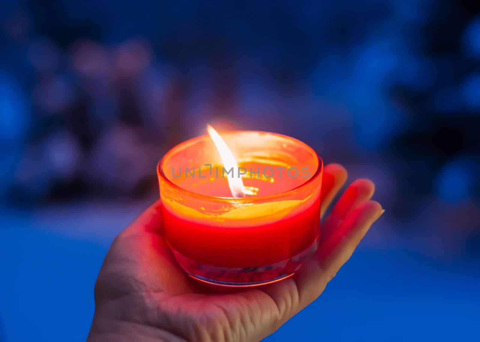 Burning red candle in a hand on winter background