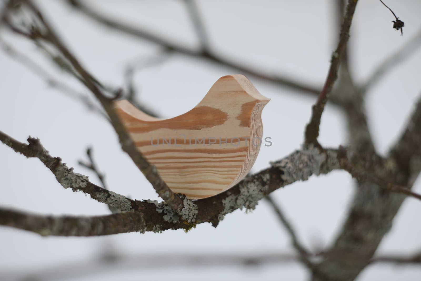 Wooden handmade toy bird on the tree branch on a winter day. Hello Spring concept. Winter landscape