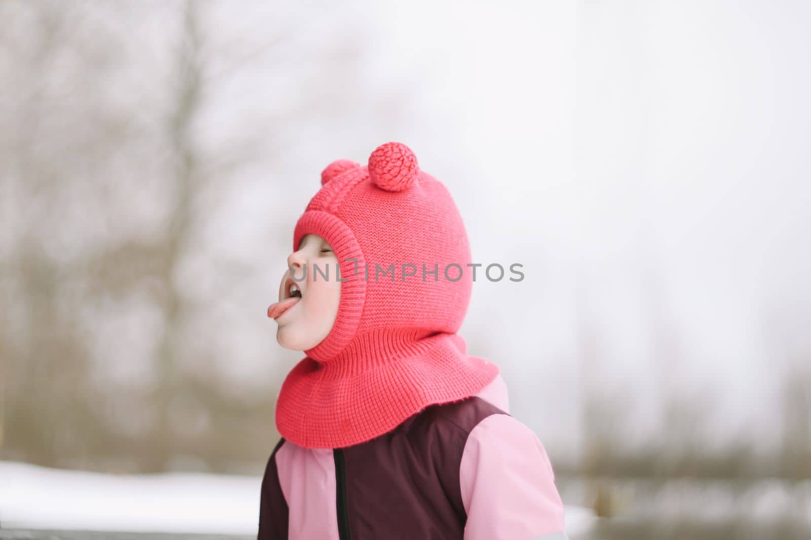 Funny little girl eating snow on winter day. Kids cold and flu concept. Tongue in snow