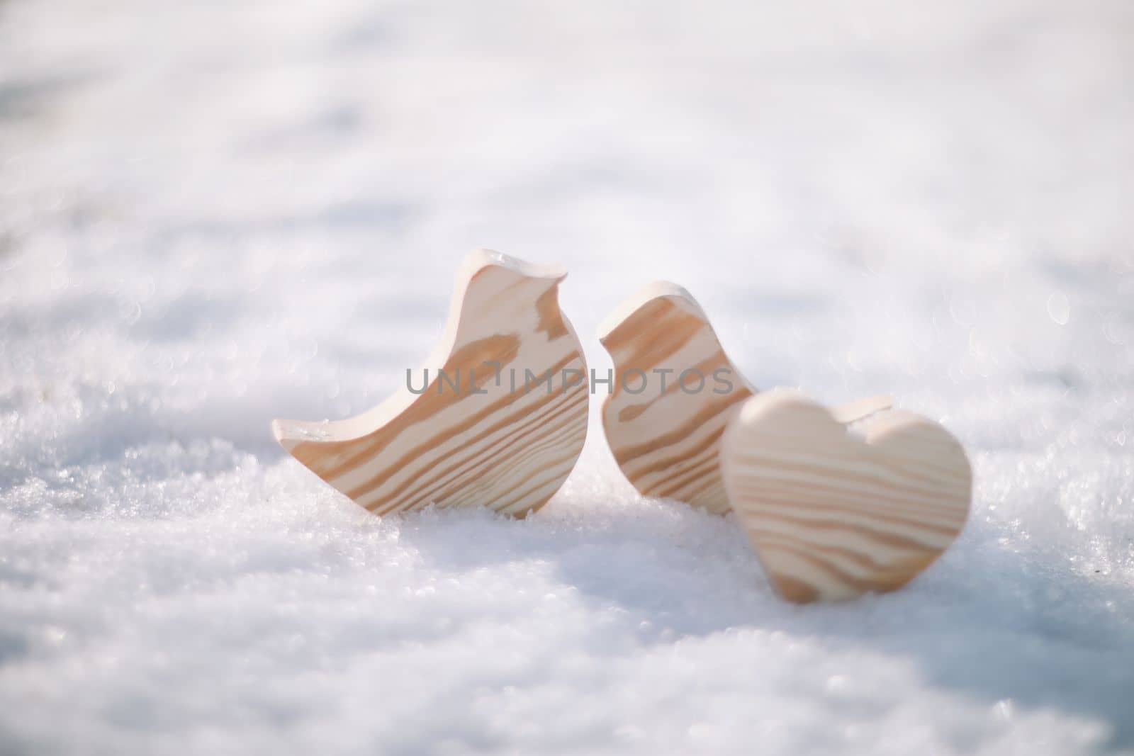 Beautiful decorative small wooden toy birds on white snow in winter. Easter, Spring decoration. Handmade wooden toys.