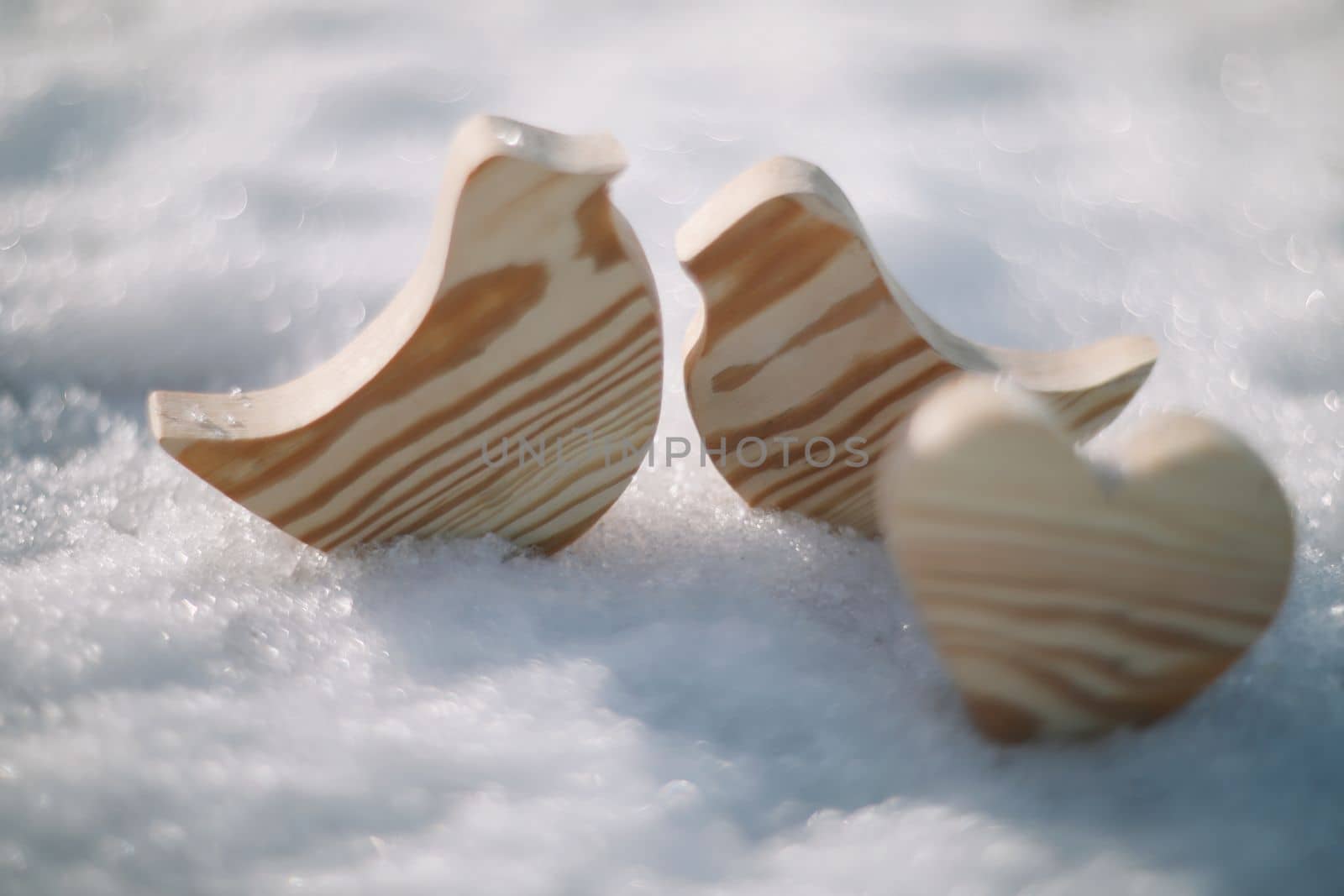 Beautiful decorative small wooden toy birds on white snow in winter. Easter, Spring decoration. Handmade wooden toys.
