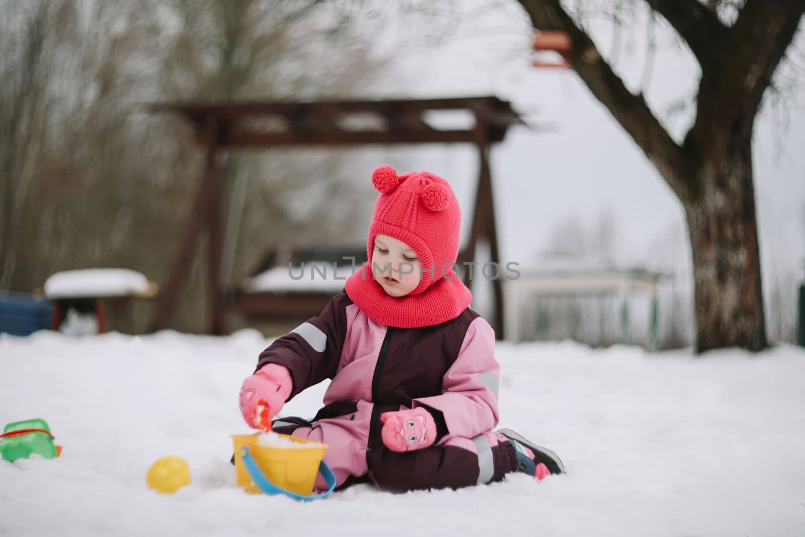 Adorable girl dig snow with shovel and pail on playground covered with snow. little girl playing in the snow.