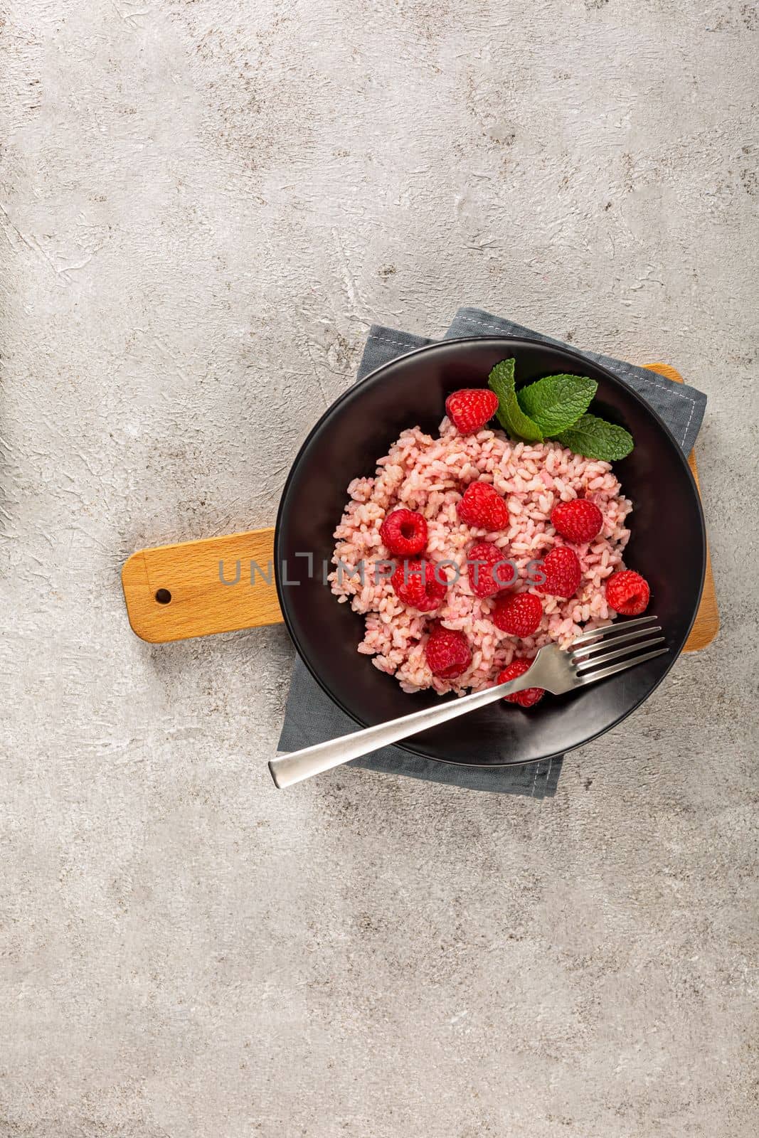 Healthy food on gray concrete background. Fresh raspberries risotto on a delicate and elegant dish. Vertical orientation. Space for text.