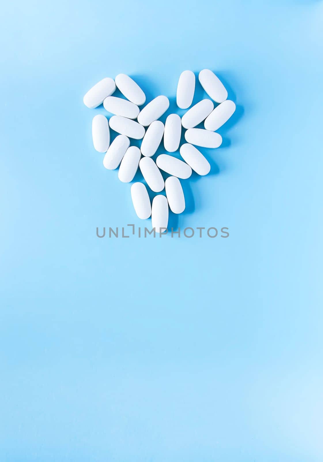 Pills of vitamin in the shape of heart on soft blue background