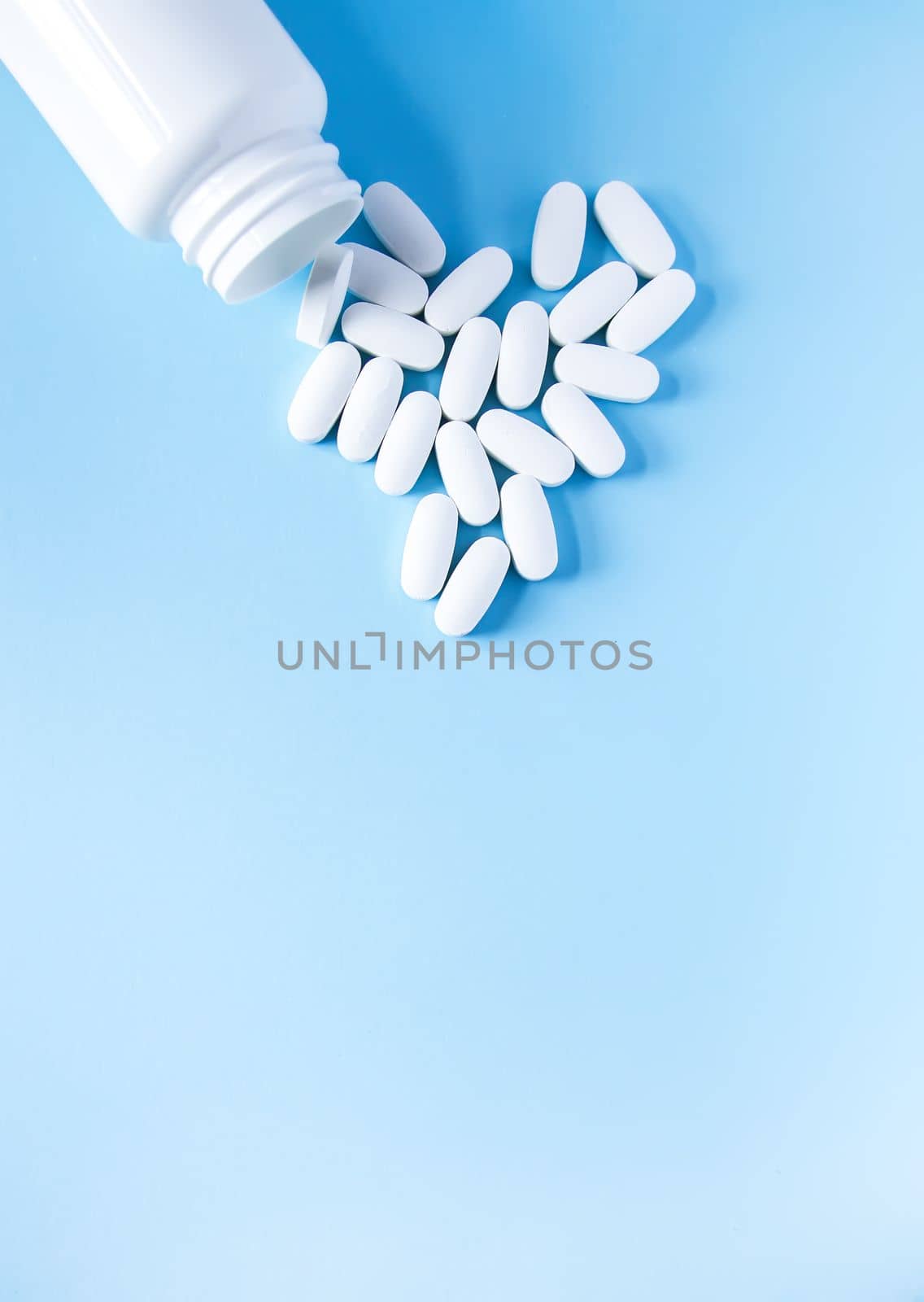Pills of vitamin in the shape of heart with the opened white plastic container on soft blue background. by nightlyviolet