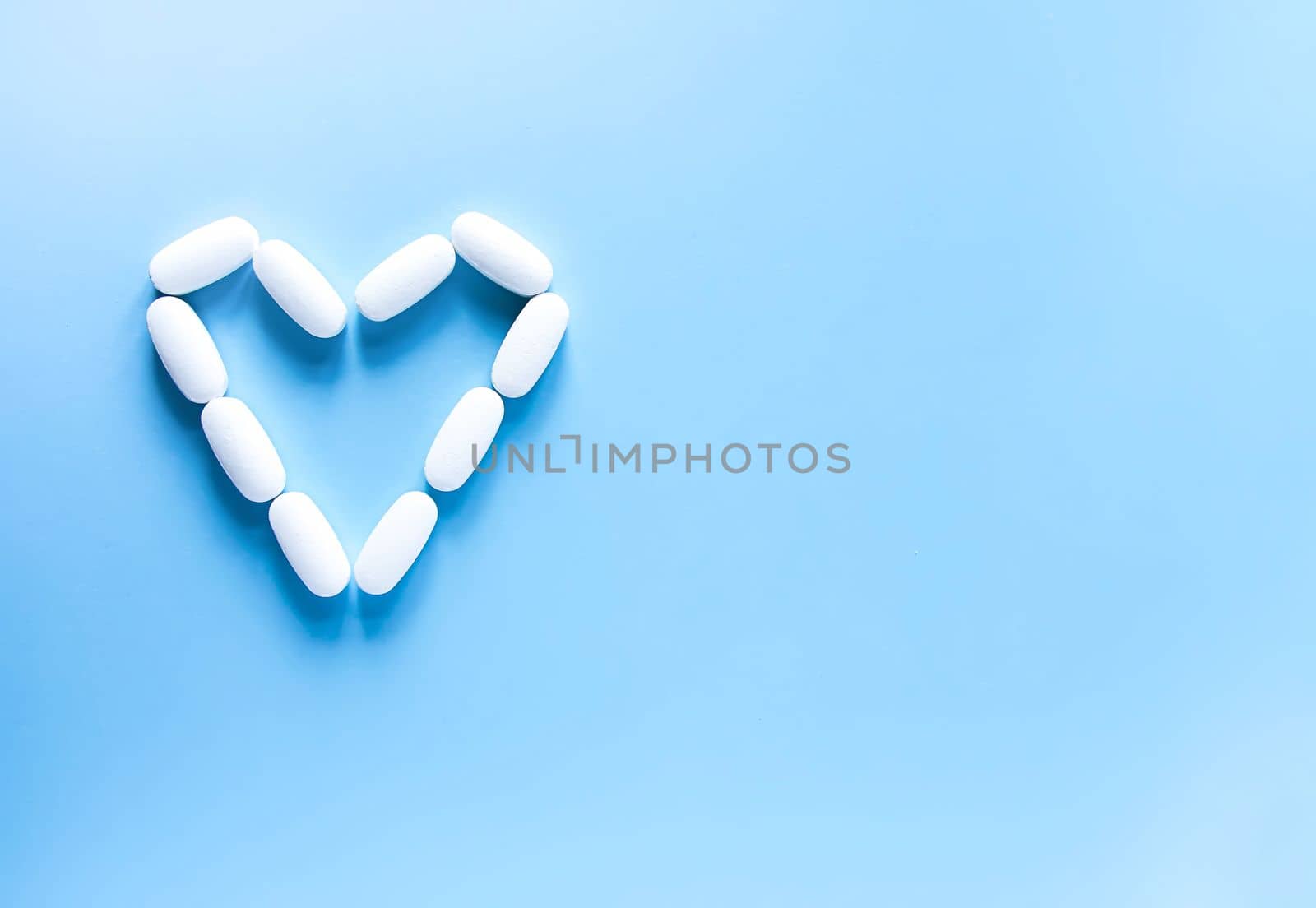 Pills of vitamin in the shape of heart on soft blue background.