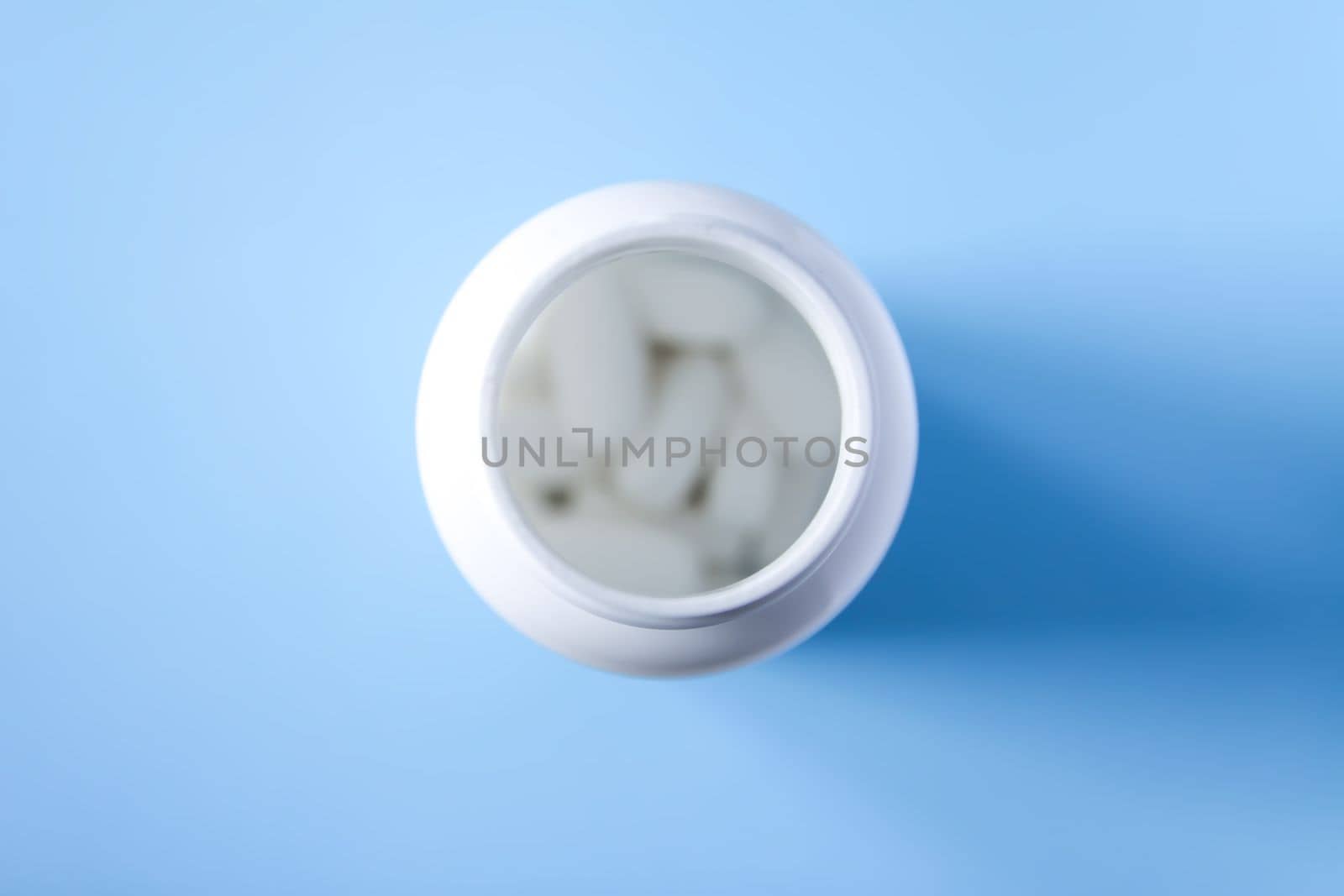 Pills of vitamin in the opened white plastic container on soft blue background. by nightlyviolet