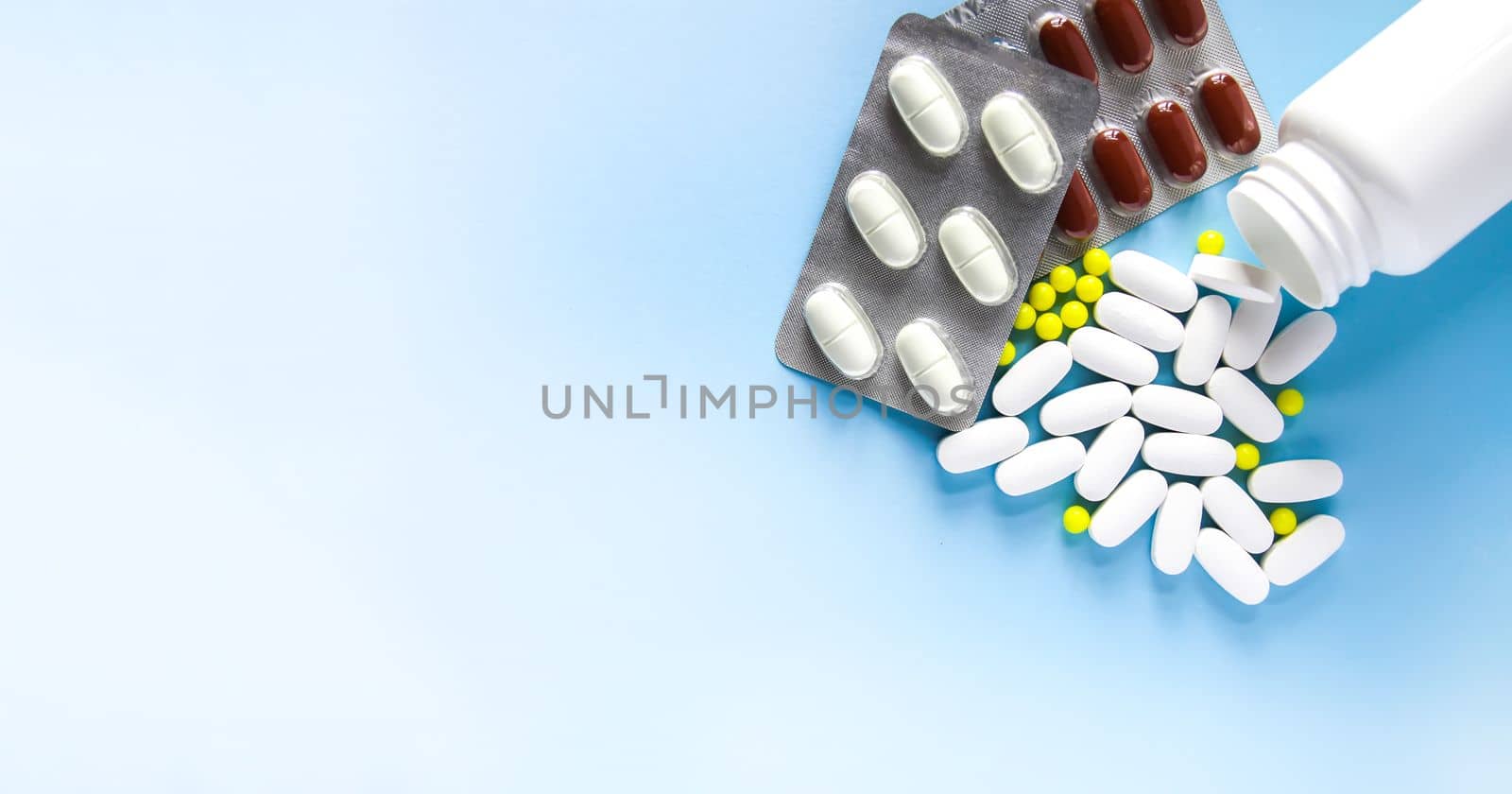 Pills of vitamin with the opened white plastic container on soft blue background