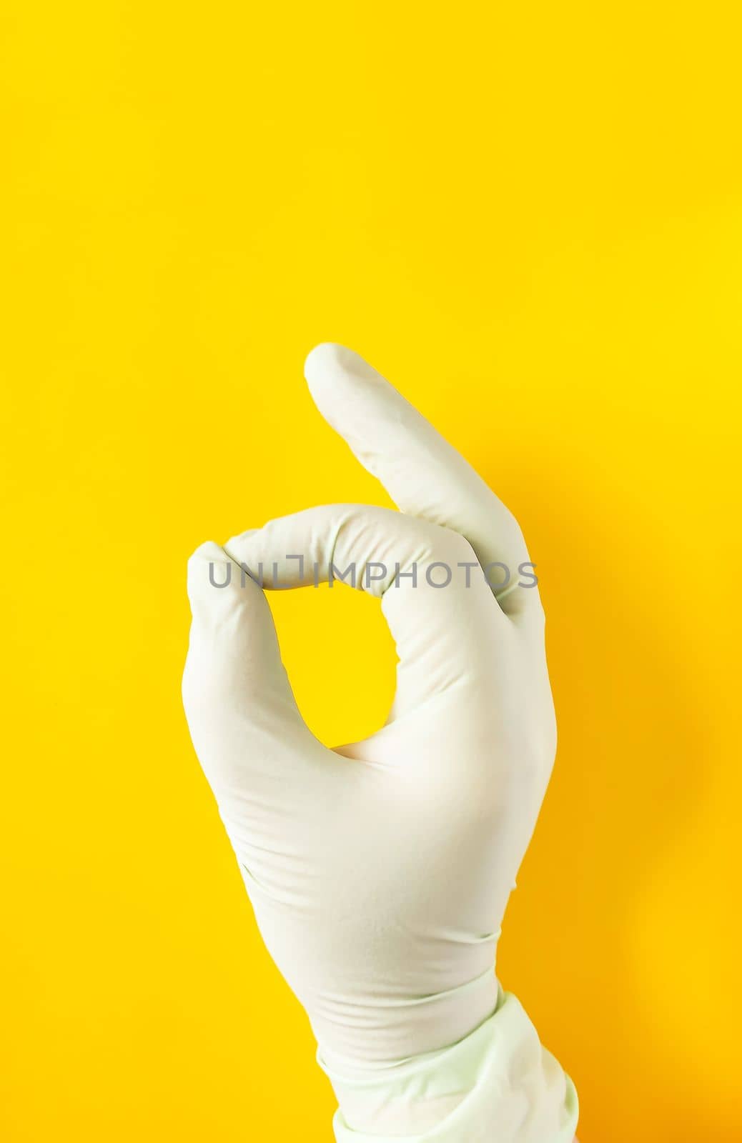 Hand in rubber glove. OK sign on bright yellow background
