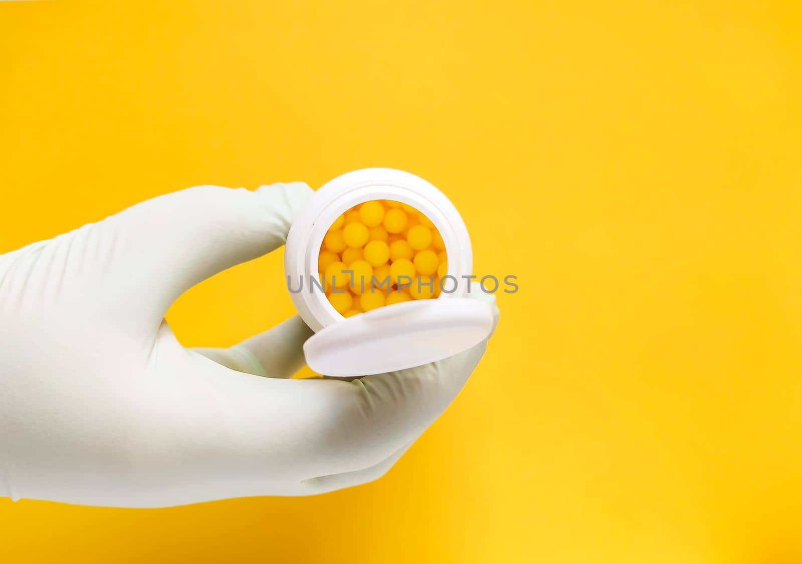 Hand in rubber glove holds vitamin C pills in a white plastic storage on bright yellow background. by nightlyviolet