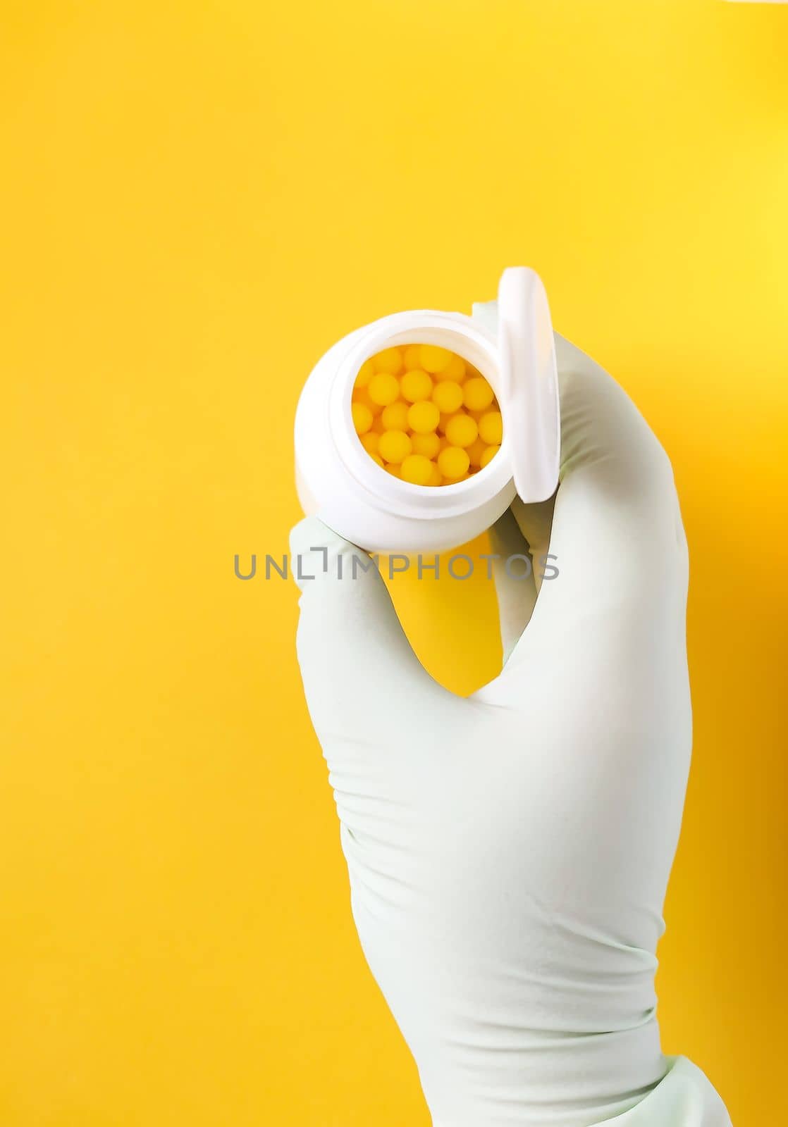 Hand in rubber glove holds vitamin C pills in a white plastic storage on bright yellow background