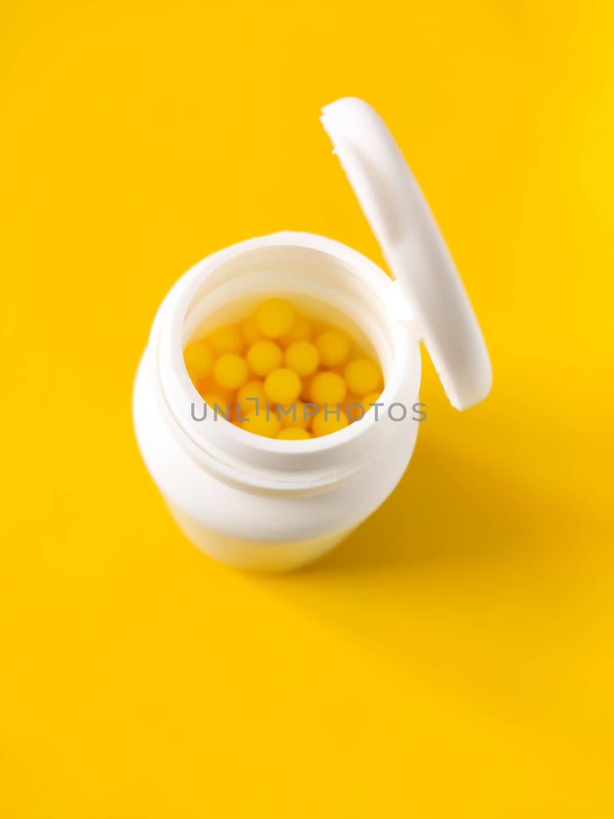 Pills of vitamin C in the opened white plastic container on bright yellow background