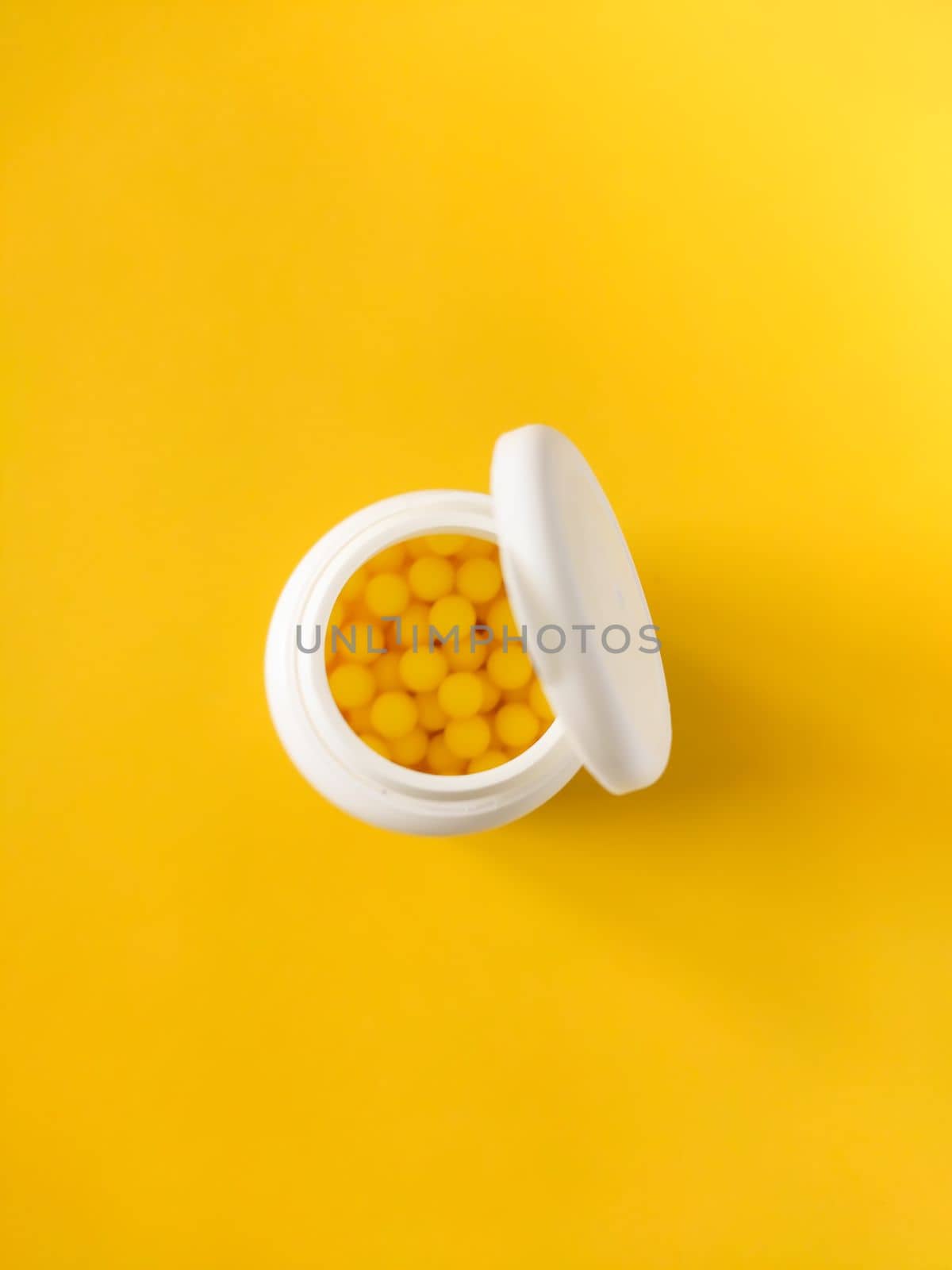 Pills of vitamin C in the opened white plastic container on bright yellow background