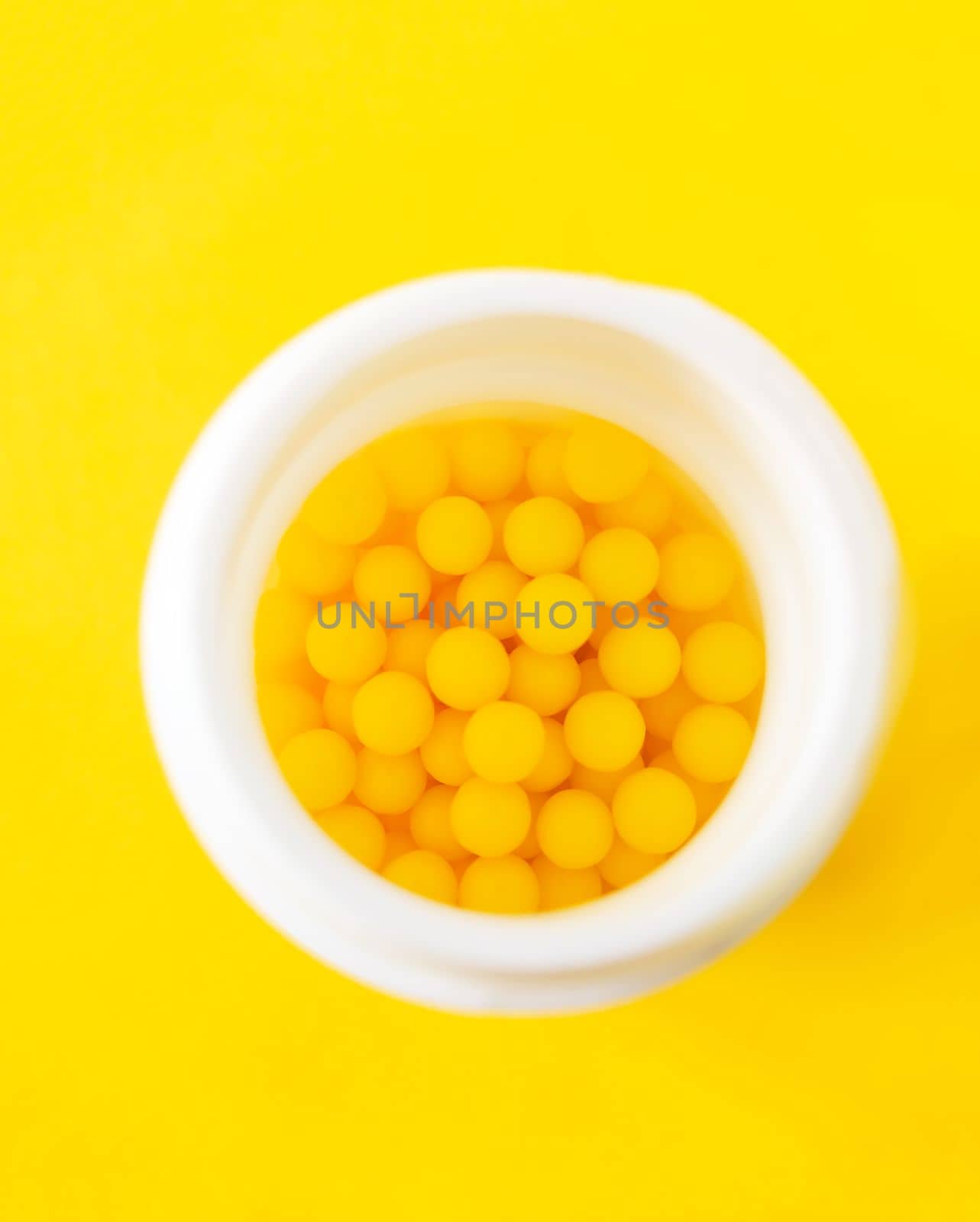 Pills of vitamin C in the opened white plastic container on bright yellow background. by nightlyviolet