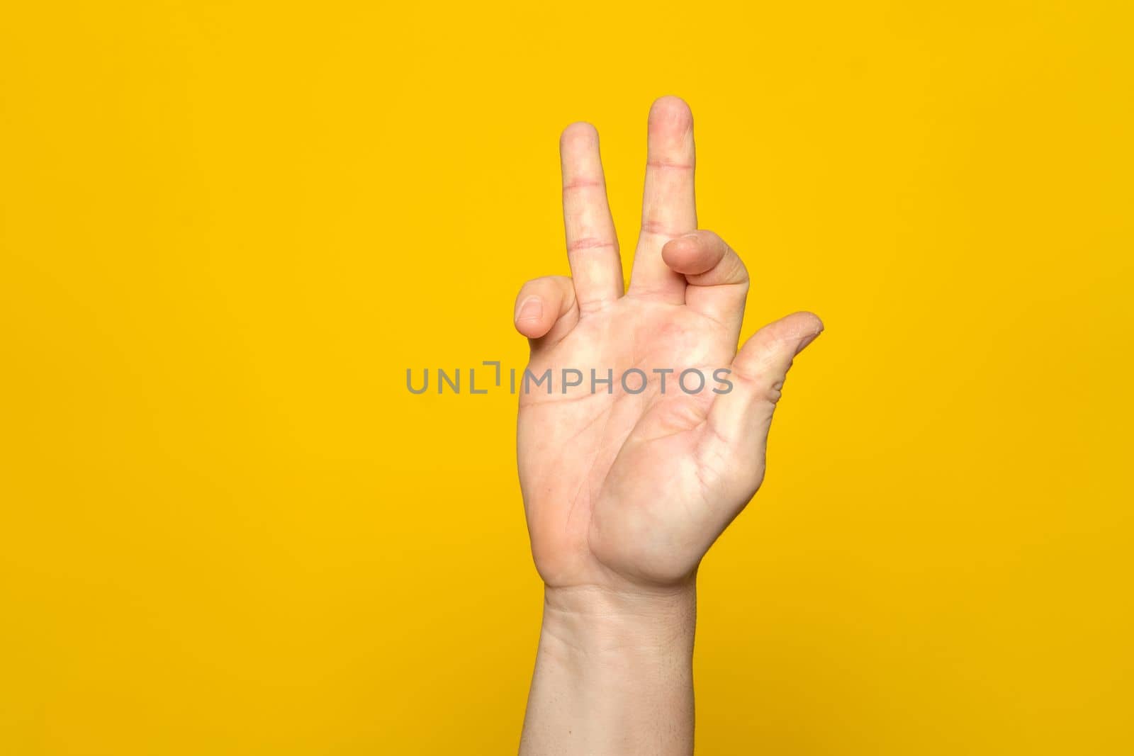 Tough man's hand making a strange and complicated gesture with his hand. It can represent a surfer, gippie or meditation gesture isolated on yellow background