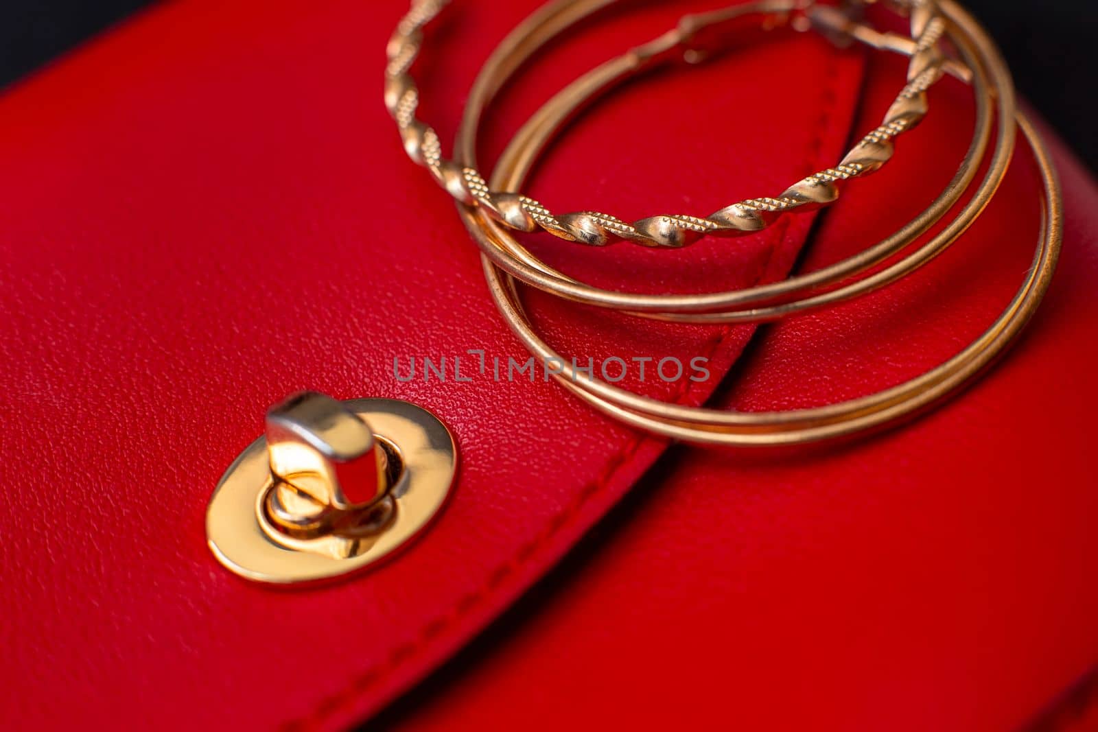 Three gold hoop earrings lie on a red leather bag. Close up. Copy space