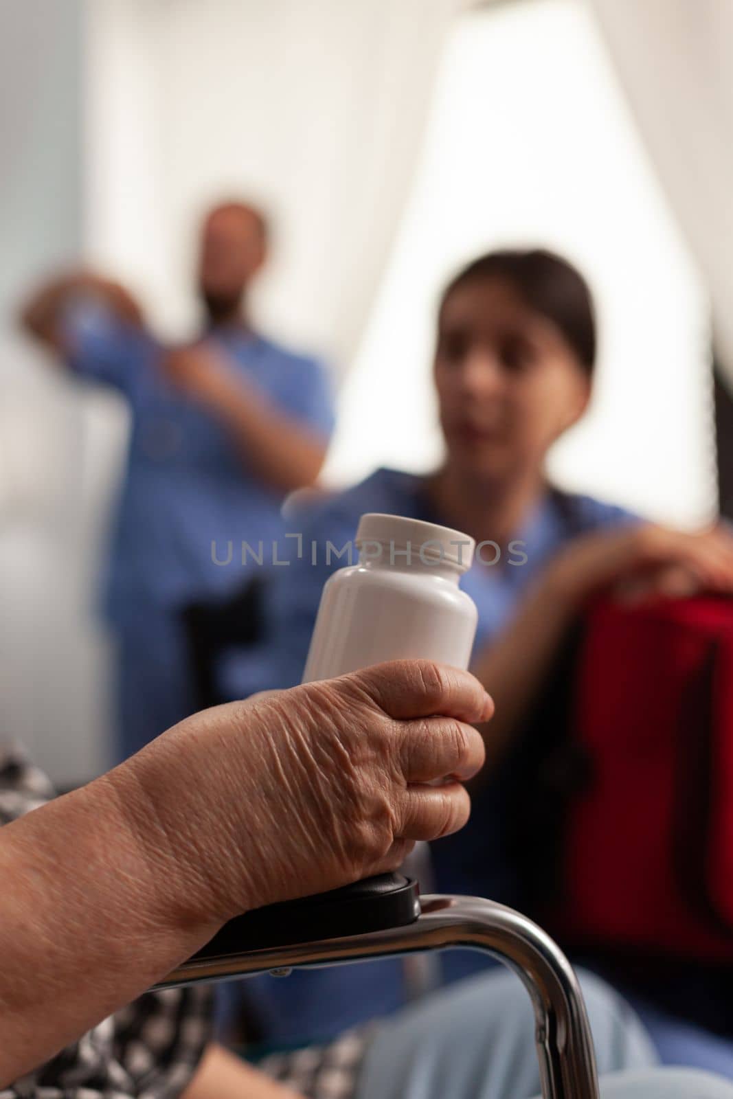 Retired woman in wheelchair holding bottle of vitamins while talking to nurse specialized in elderly care. Nurse instructing female patient with disability to take her medications correctly.