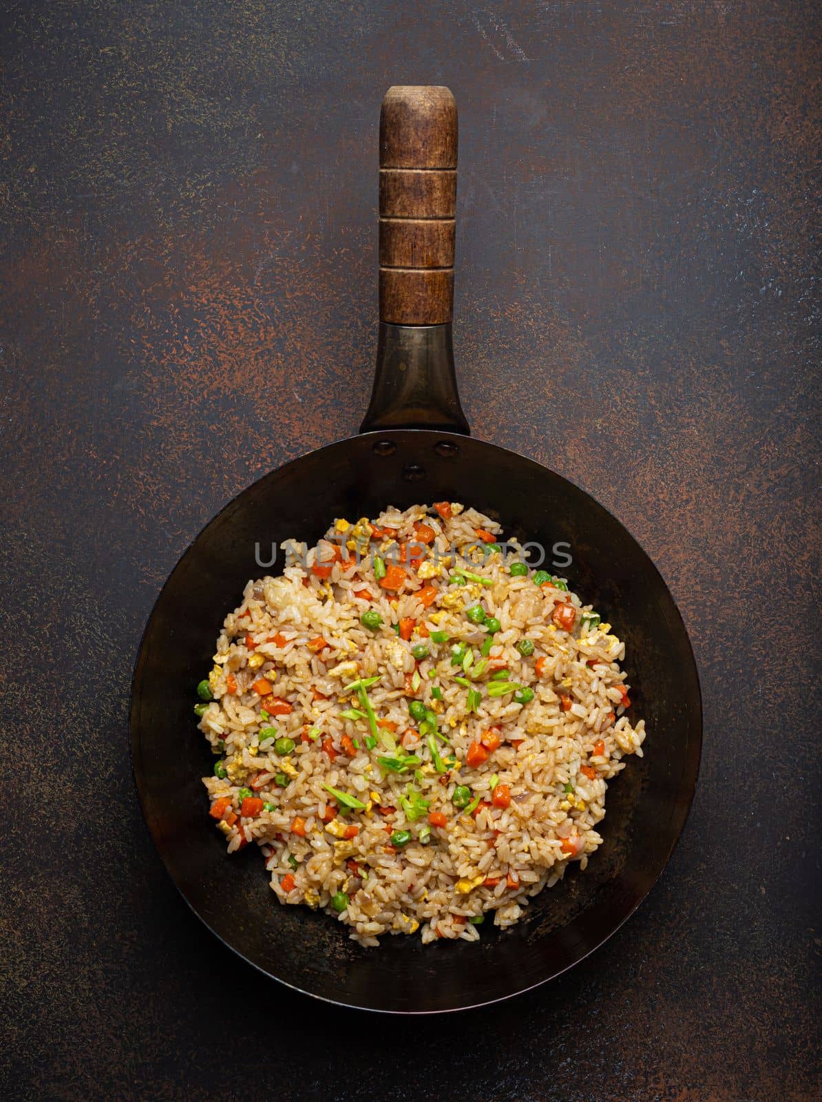 Authentic Chinese and Asian fried rice with egg and vegetables in wok top view, rustic concrete table background. Traditional dish of China by its_al_dente