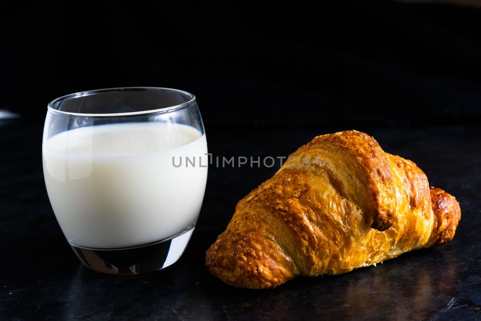 Fresh white bread and milk in white glass on black stone table background. Top view Studio shot