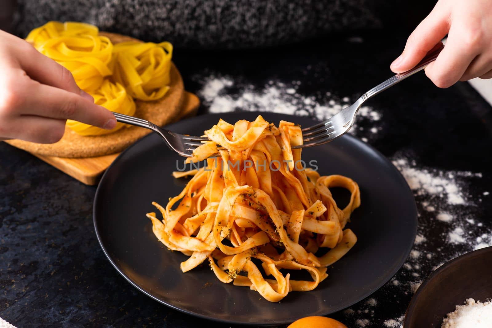 A close-up of hands holding fork, digging into a plate of fast food in a kitchen.