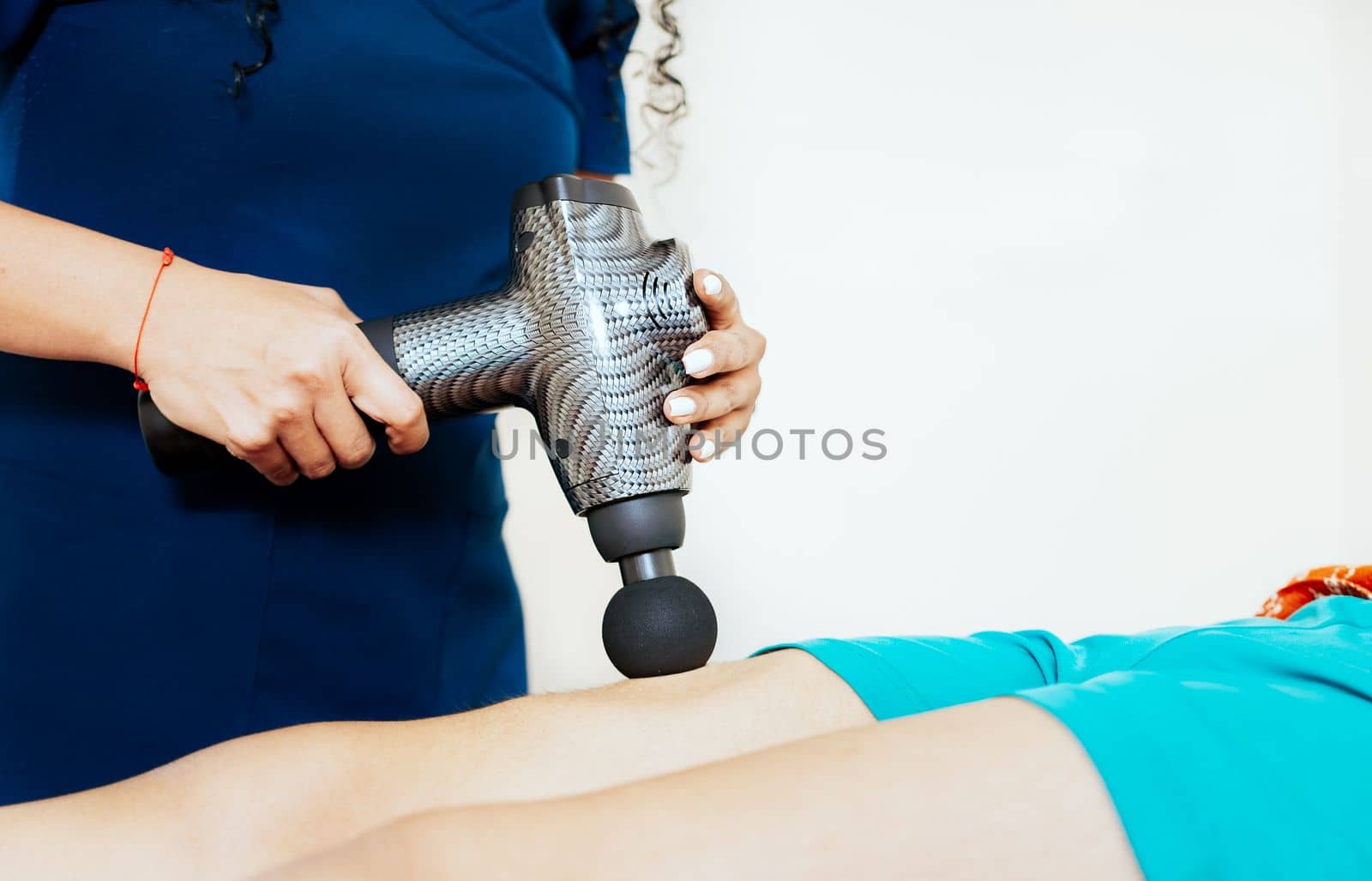 Physiotherapist using massage gun on female patient. Physiotherapist hand using massage gun on patient. Chiropractor using massage gun on patient leg with copy space by isaiphoto