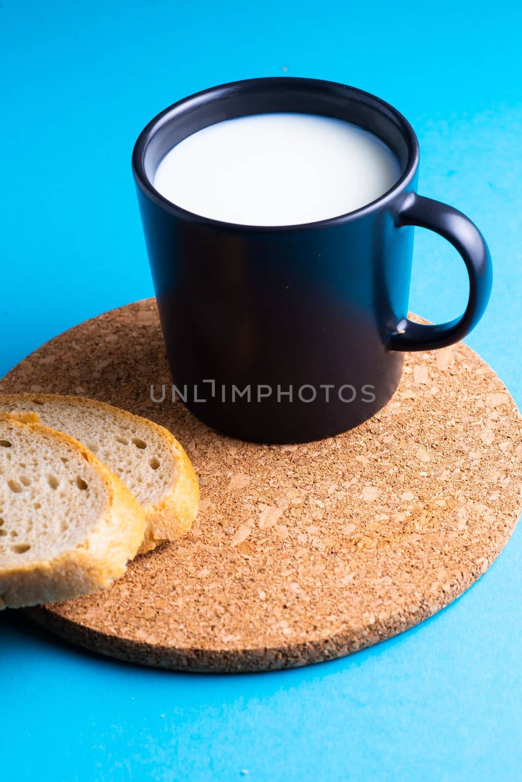 Breakfast bread and a cup of milk on yellow and blue background by Zelenin