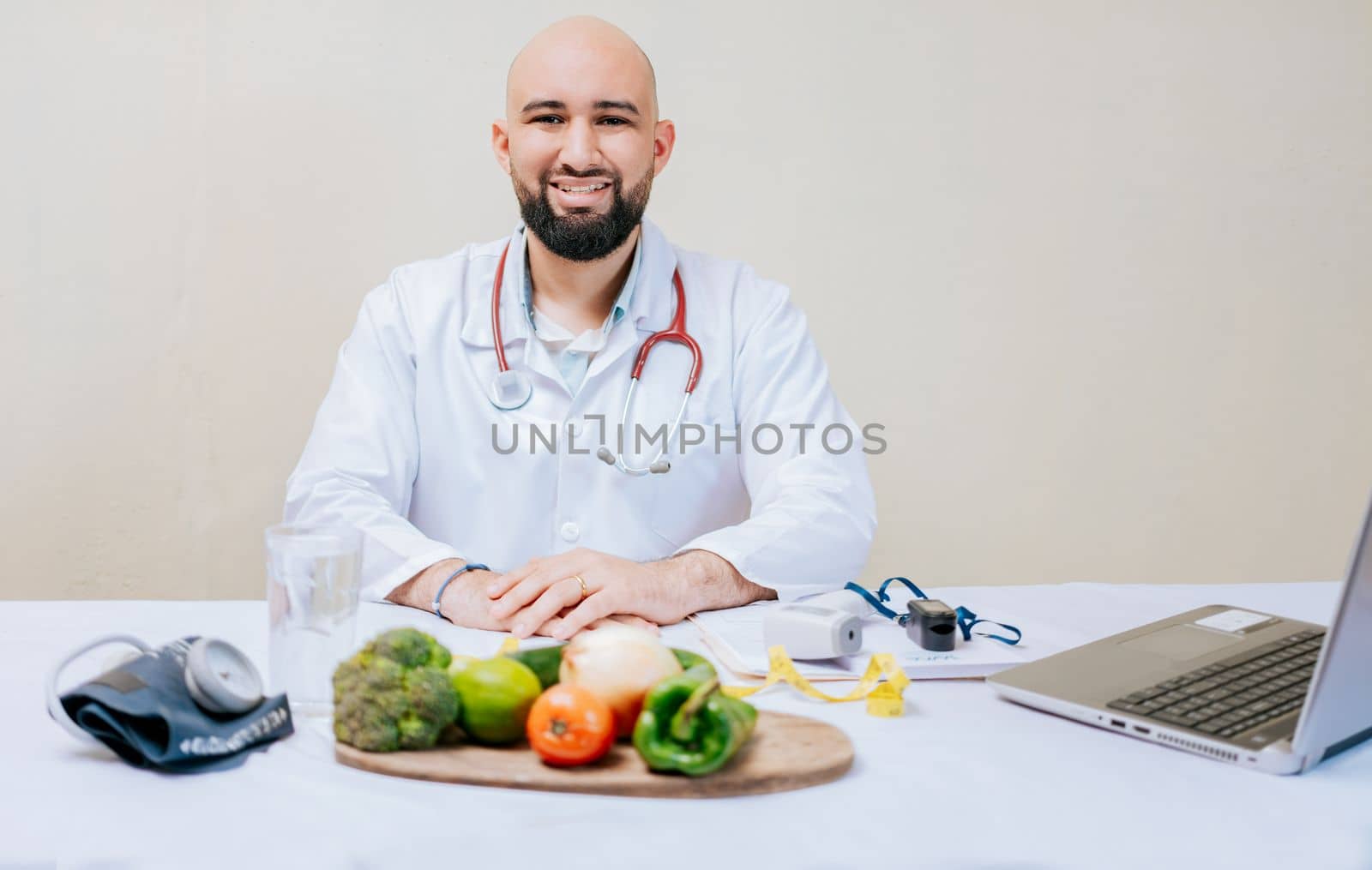 Portrait of smiling nutritionist at her desk. Smiling nutritionist doctor at desk with laptop and vegetables. Bearded nutritionist doctor at his workplace