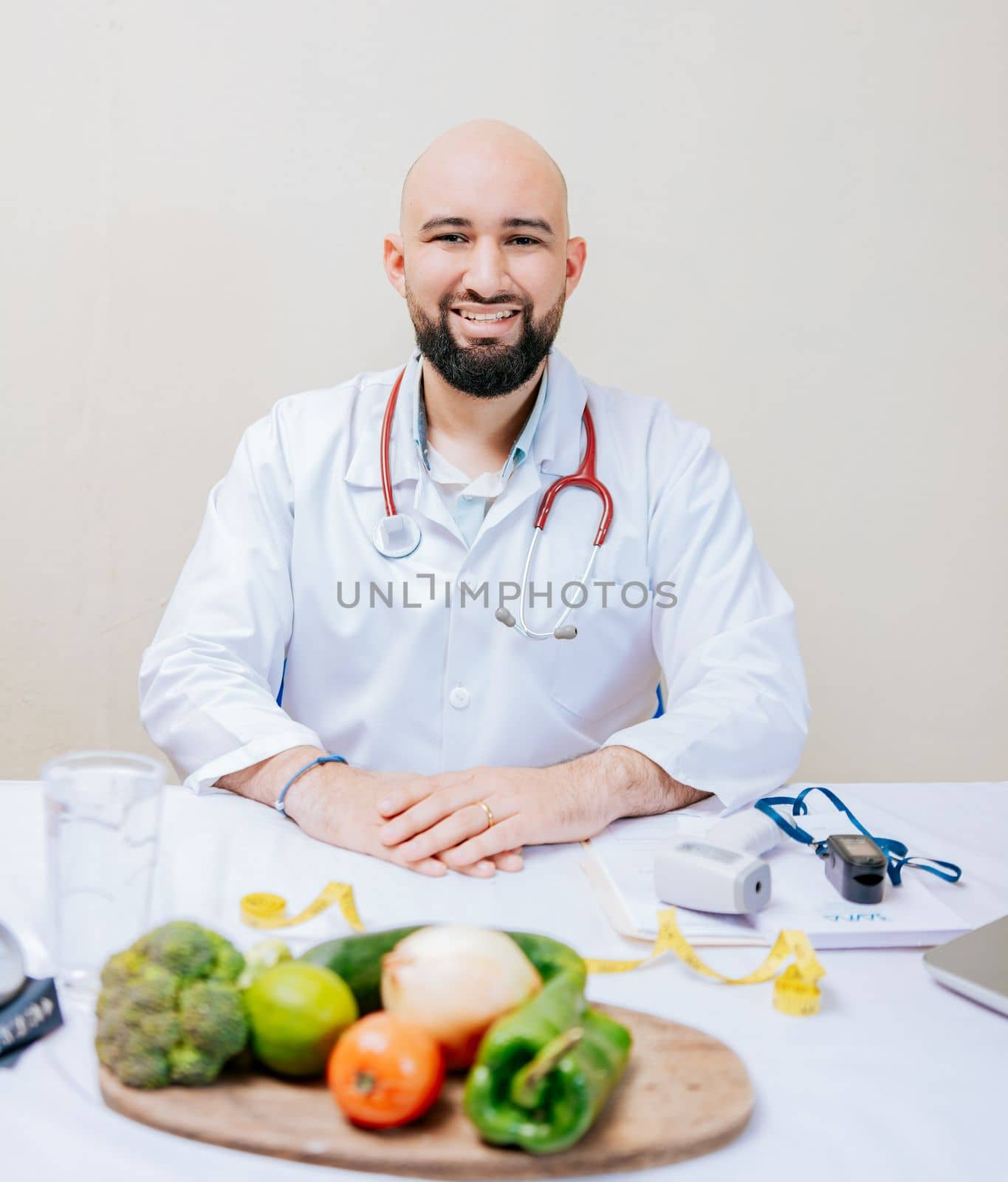 Smiling nutritionist doctor at desk with laptop and vegetables. Bearded nutritionist doctor at his workplace, Portrait of smiling nutritionist at her desk